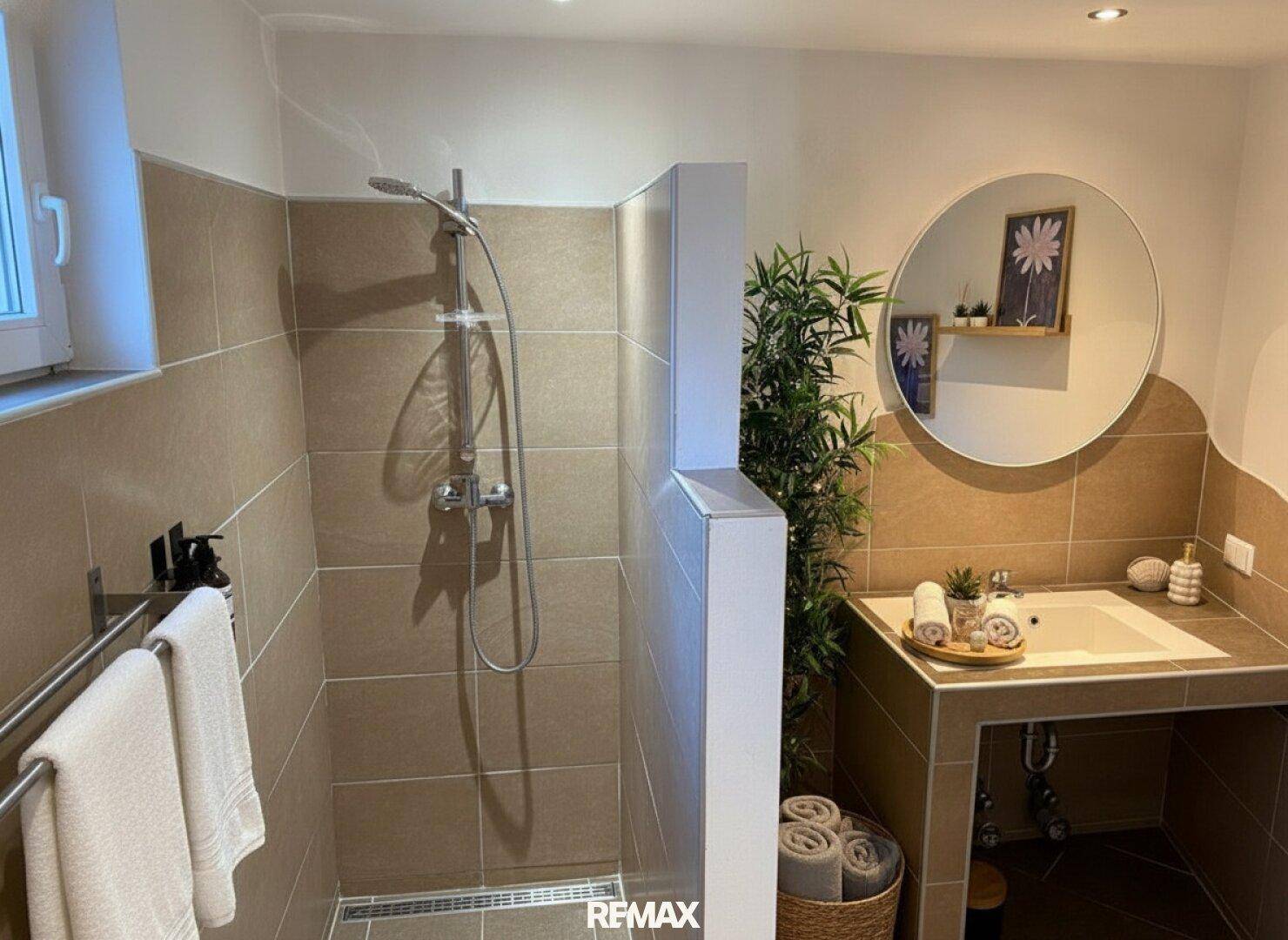 Modernes Badezimmer mit begehbarer Dusche, Einzelwaschbecken und runden Spiegel.