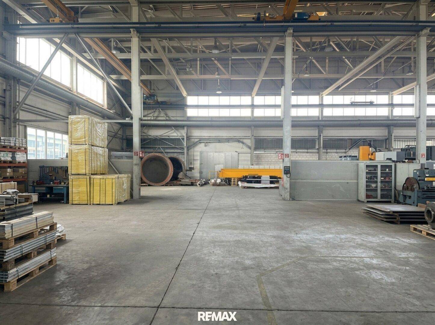 Geräumige Industriehalle mit Betonboden, großen Fenstern und verschiedenen Materialien gelagert.