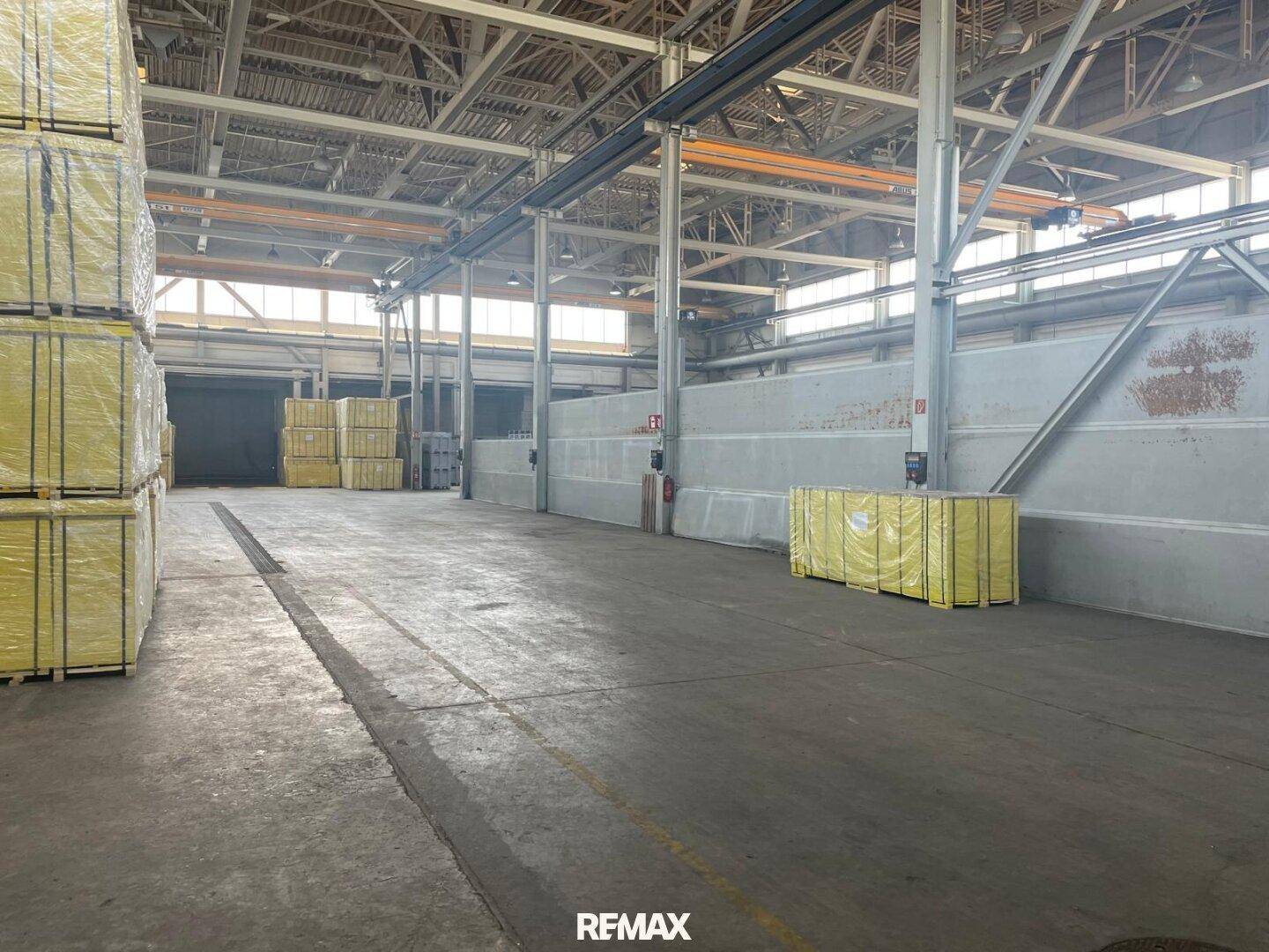 Weitläufige Industriehalle mit Betonboden, hohen Decken und gestapelten Materialien.