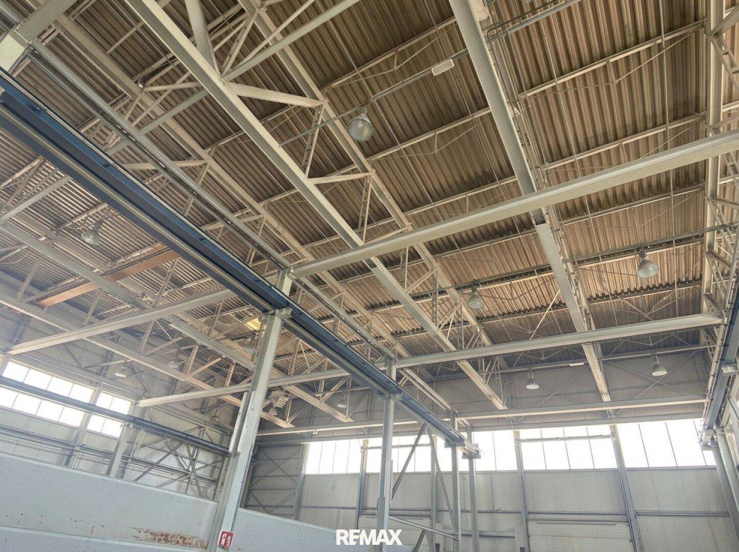 Innenansicht einer großen Industriehalle mit sichtbaren Stahlträgern und Oberlichtern.