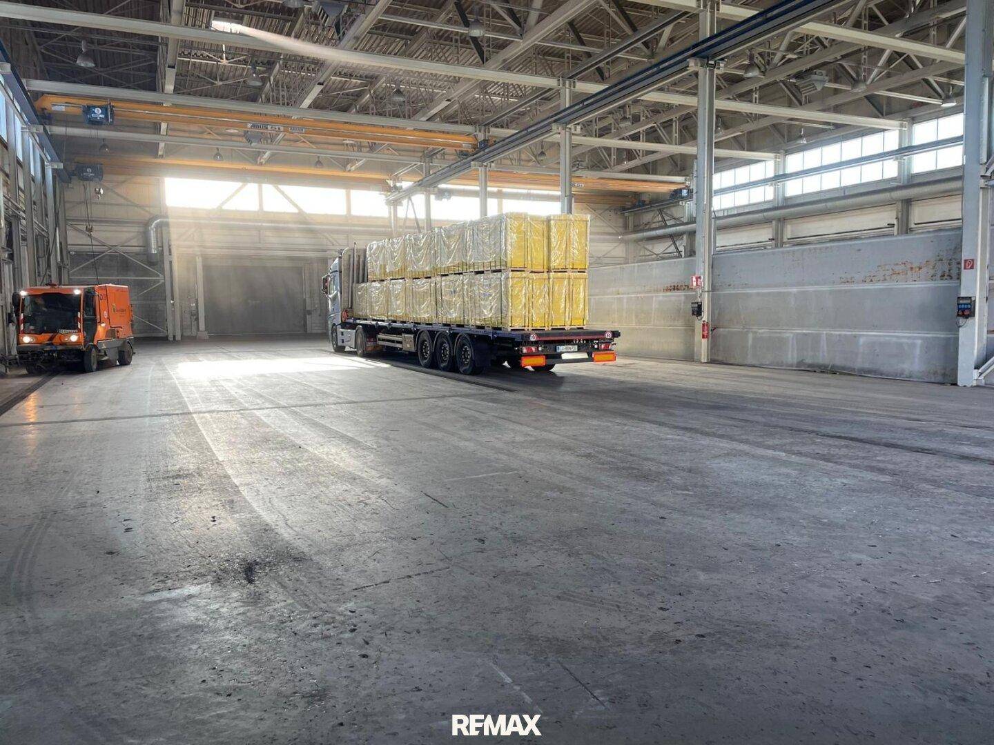 Geräumige Industriehalle mit hohen Decken, Tageslicht und einem LKW für den Warentransport.