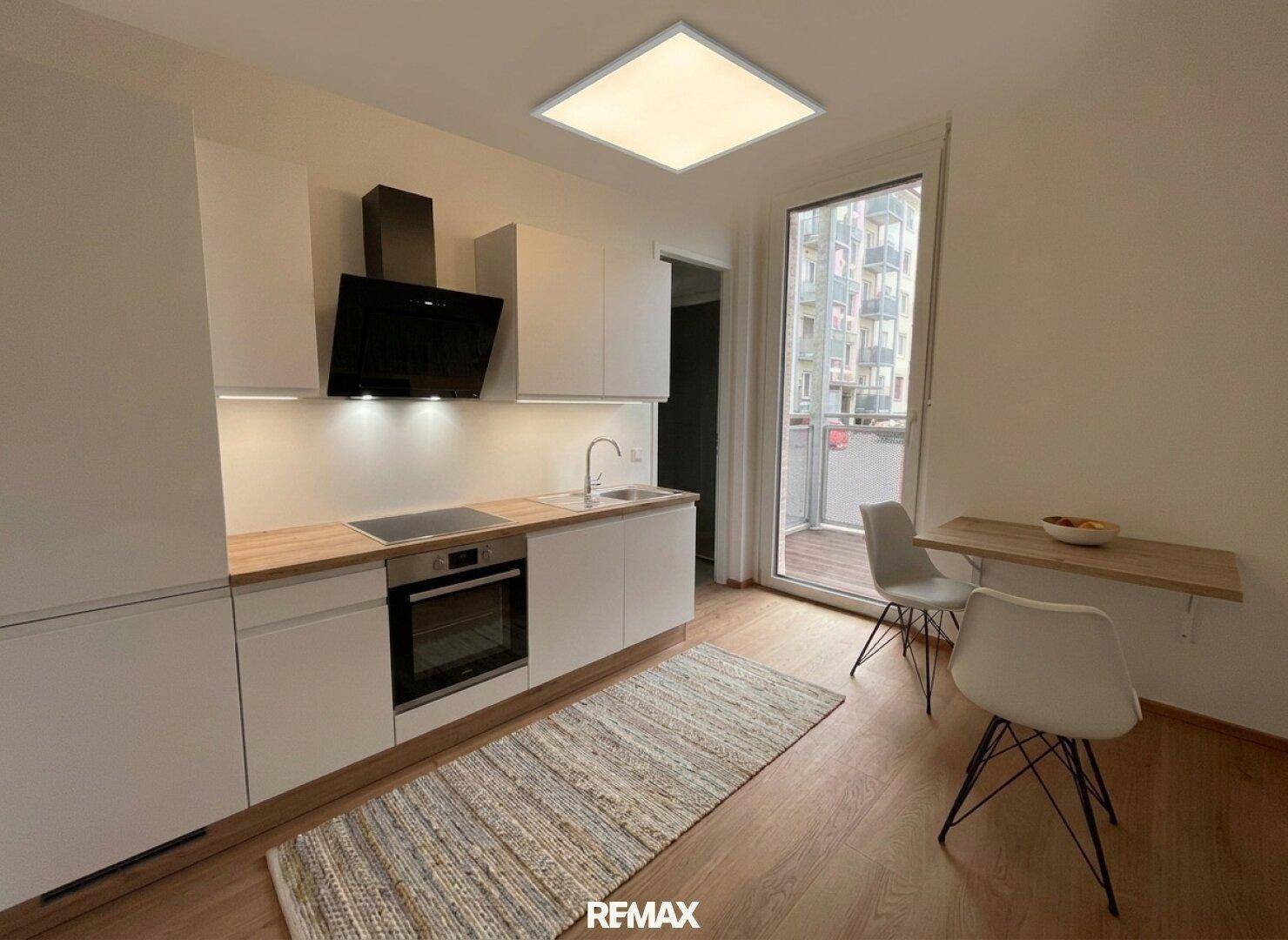 Moderne Küche mit weißen Schränken, Holzarbeitsplatte und Zugang zum Balkon.