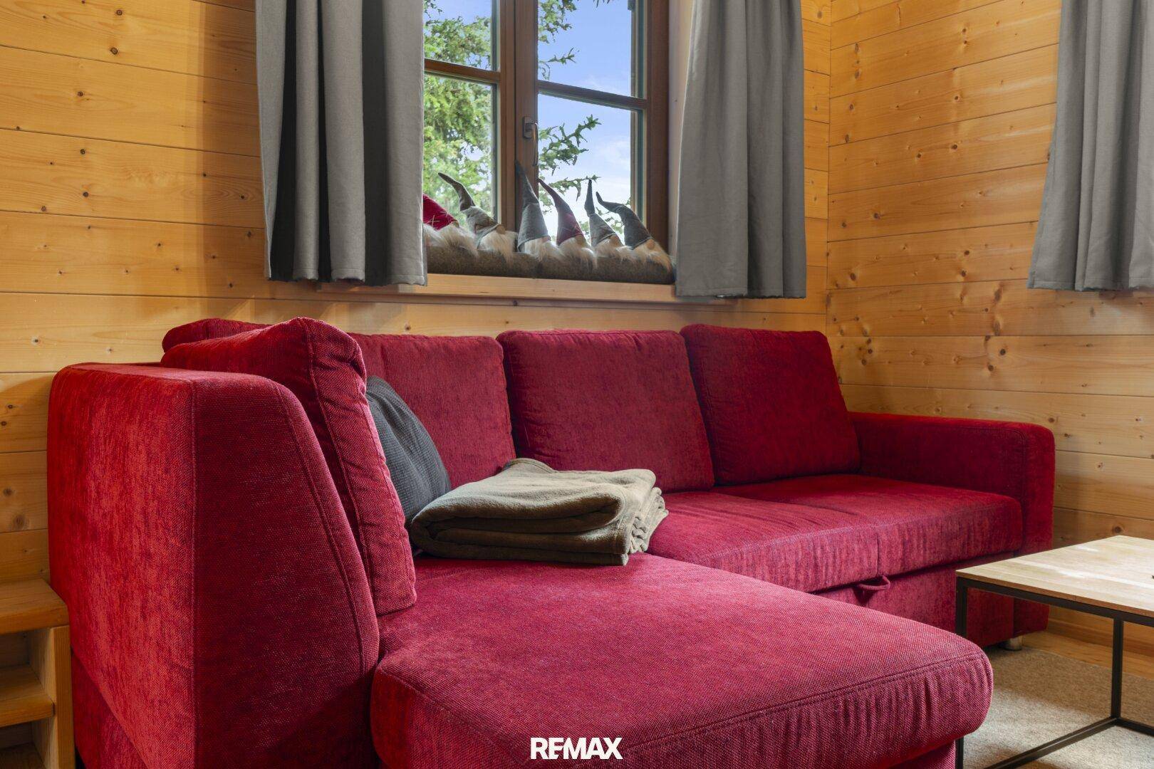Rotes Ecksofa im Wohnzimmer mit Holzwänden und Blick auf die Natur.