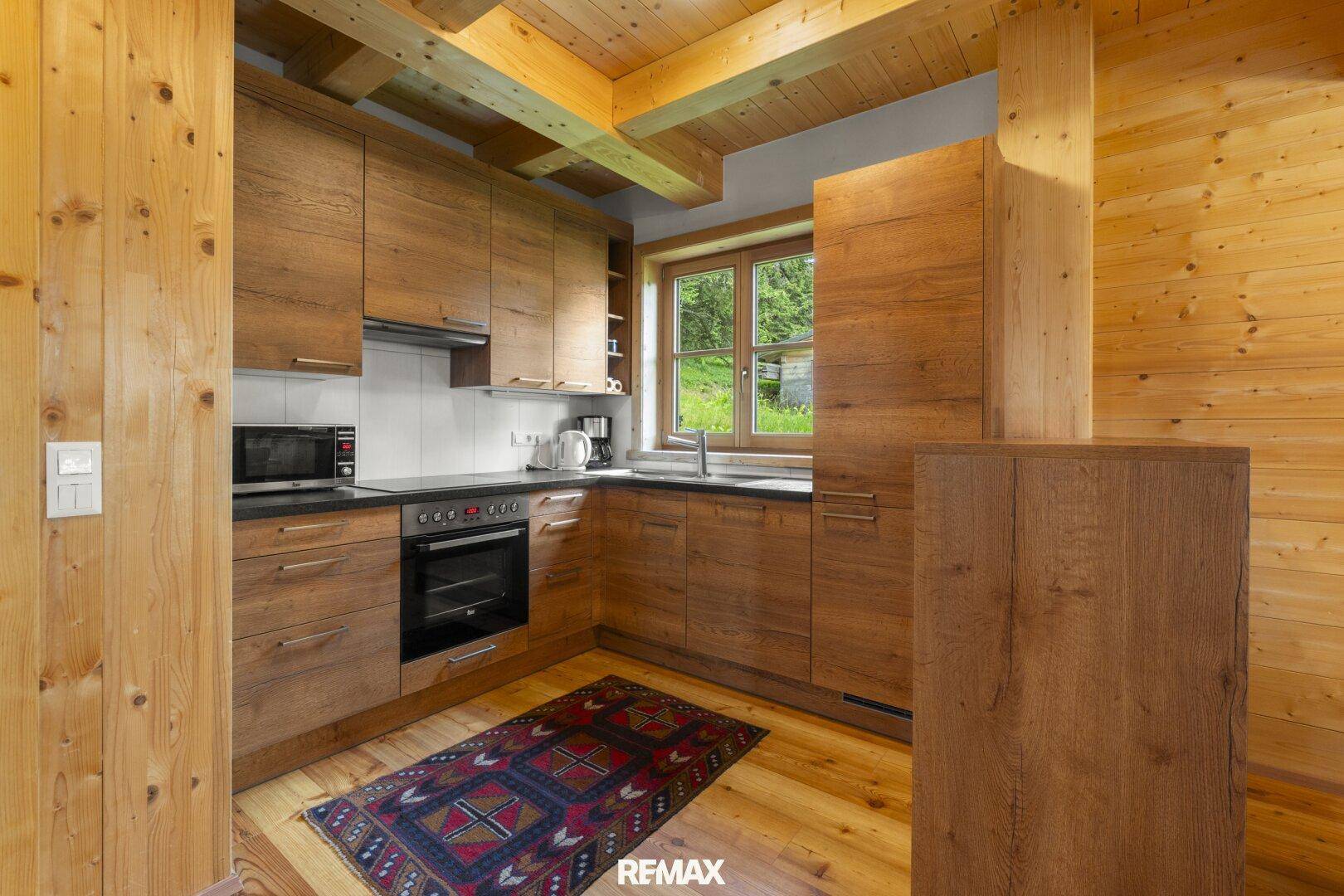 Moderne Holzküche mit Einbaugeräten, dunkler Arbeitsplatte und Blick ins Grüne.