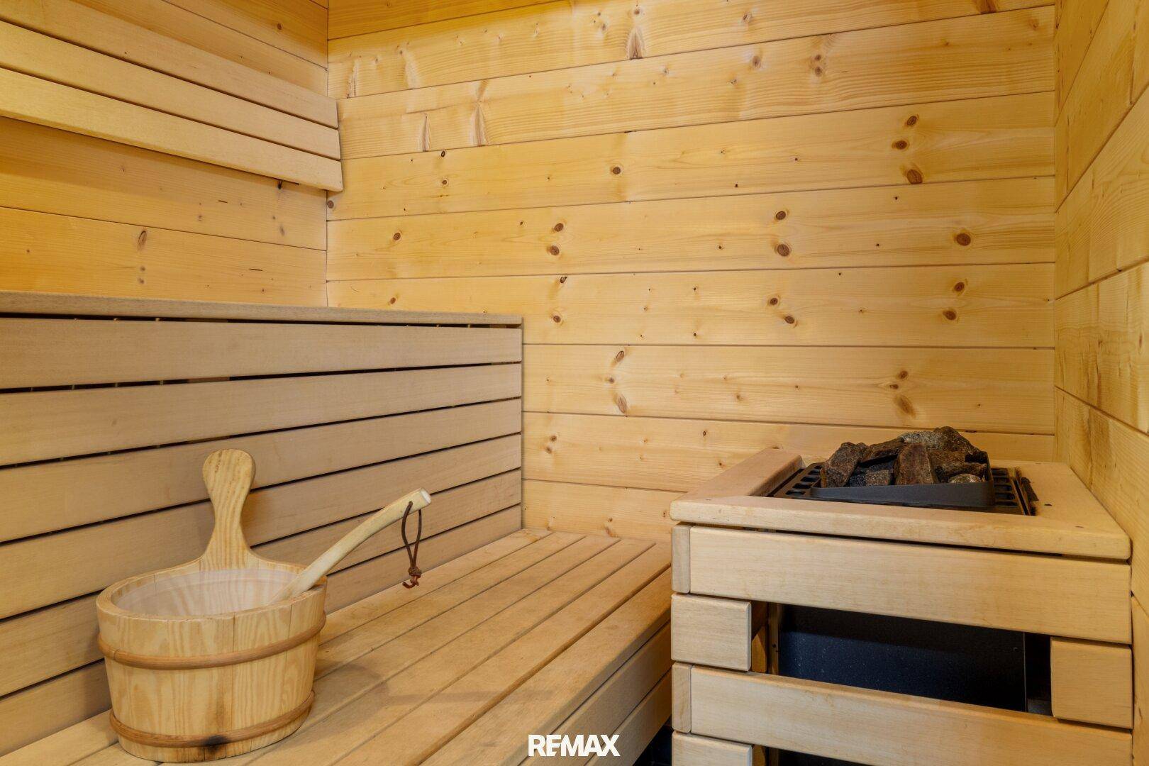 Innenansicht der Holzsauna mit traditionellem Aufgusseimer und Heizofen.