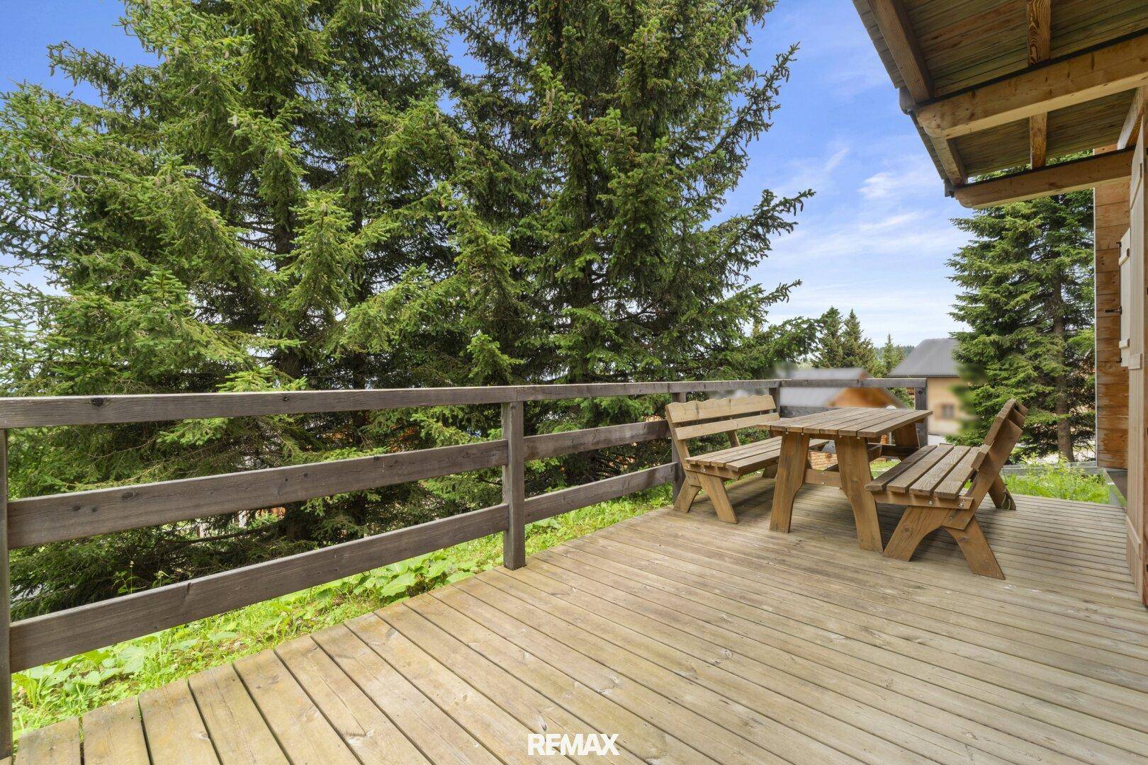 Holzterrasse mit Sitzgelegenheiten und Blick auf die umliegenden Bäume und Natur.