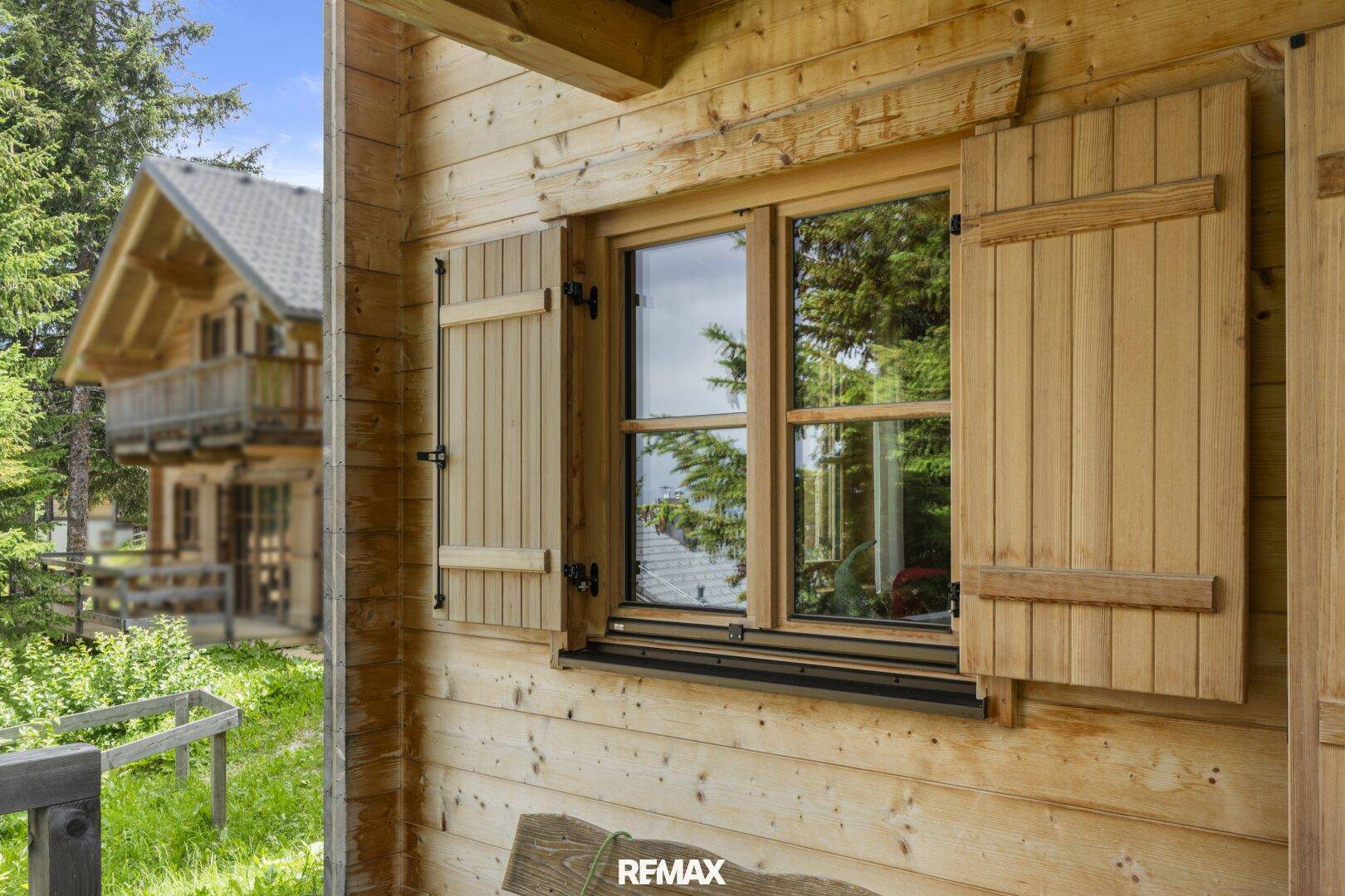 Detailansicht eines Holzfensters mit traditionellen Fensterläden an der Chaletfassade.