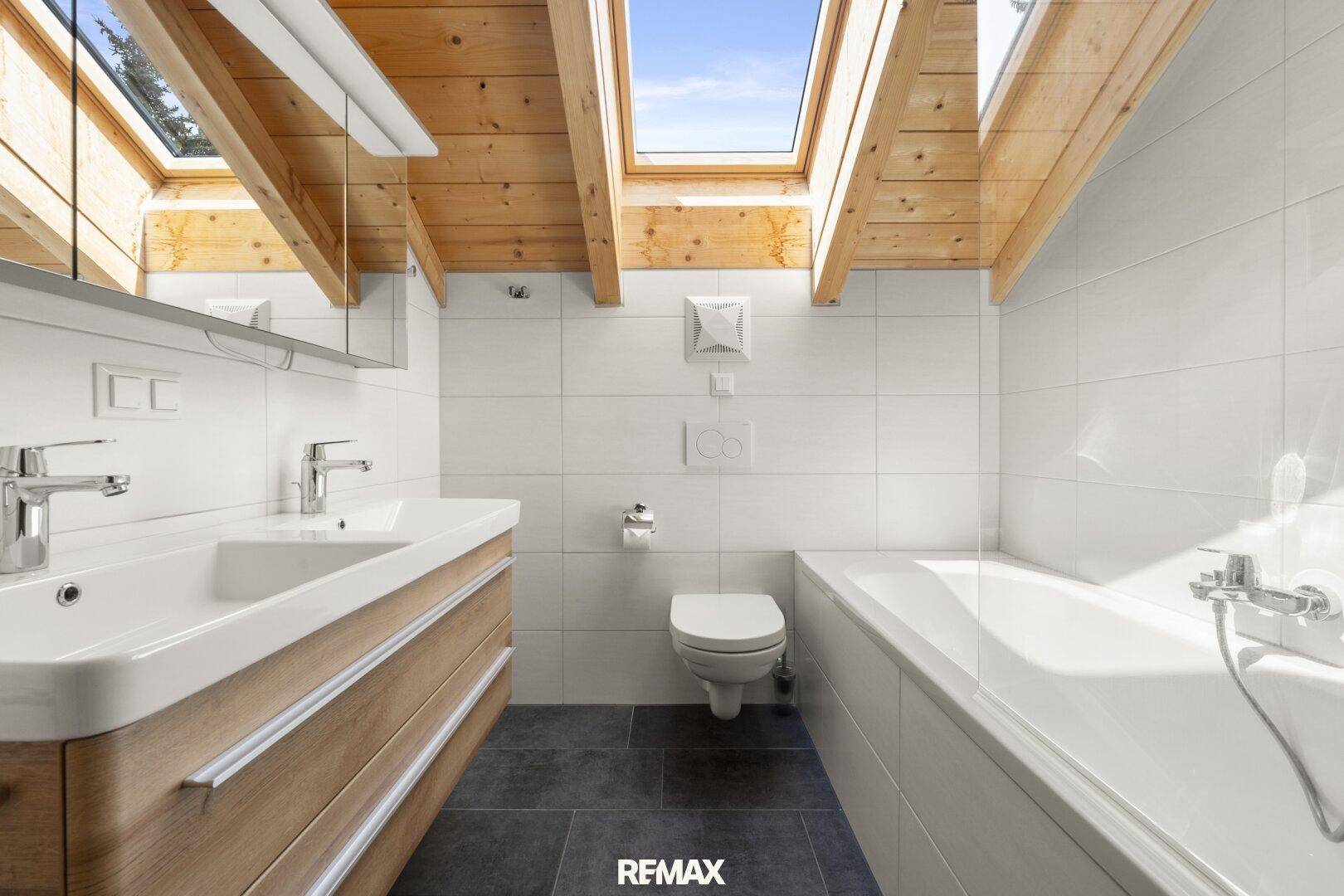 Modernes Badezimmer mit Holzbalkendecke, Dachfenstern, Badewanne und Doppelwaschbecken.