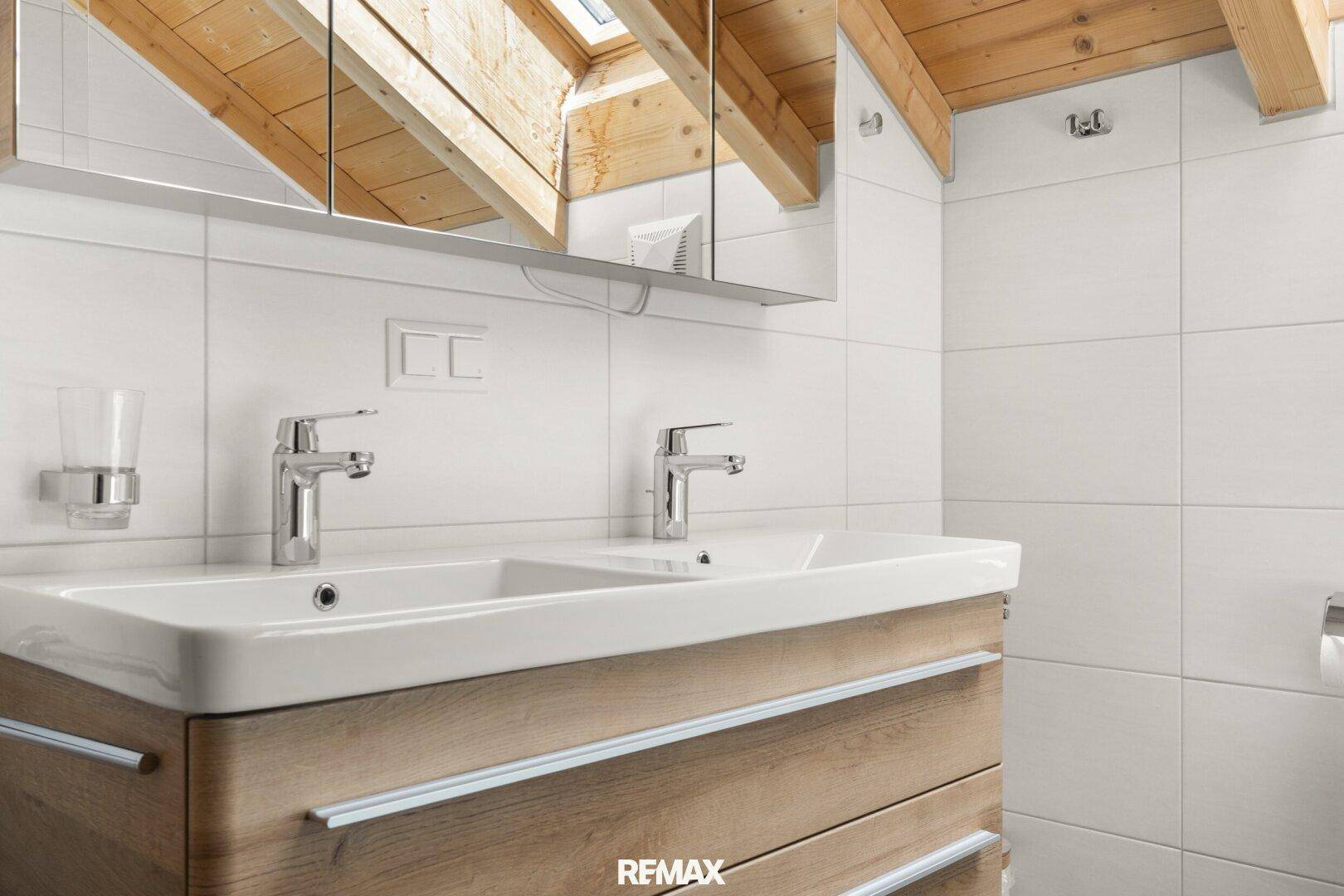 Modernes Badezimmer mit Doppelwaschbecken, Spiegelschrank und Dachfenster.