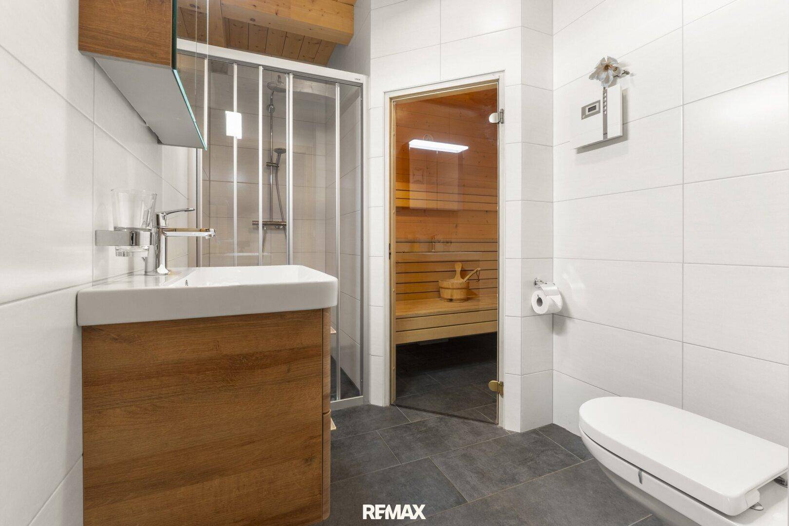 Modernes Badezimmer mit Dusche, Waschtisch und integrierter Sauna für Wellness.