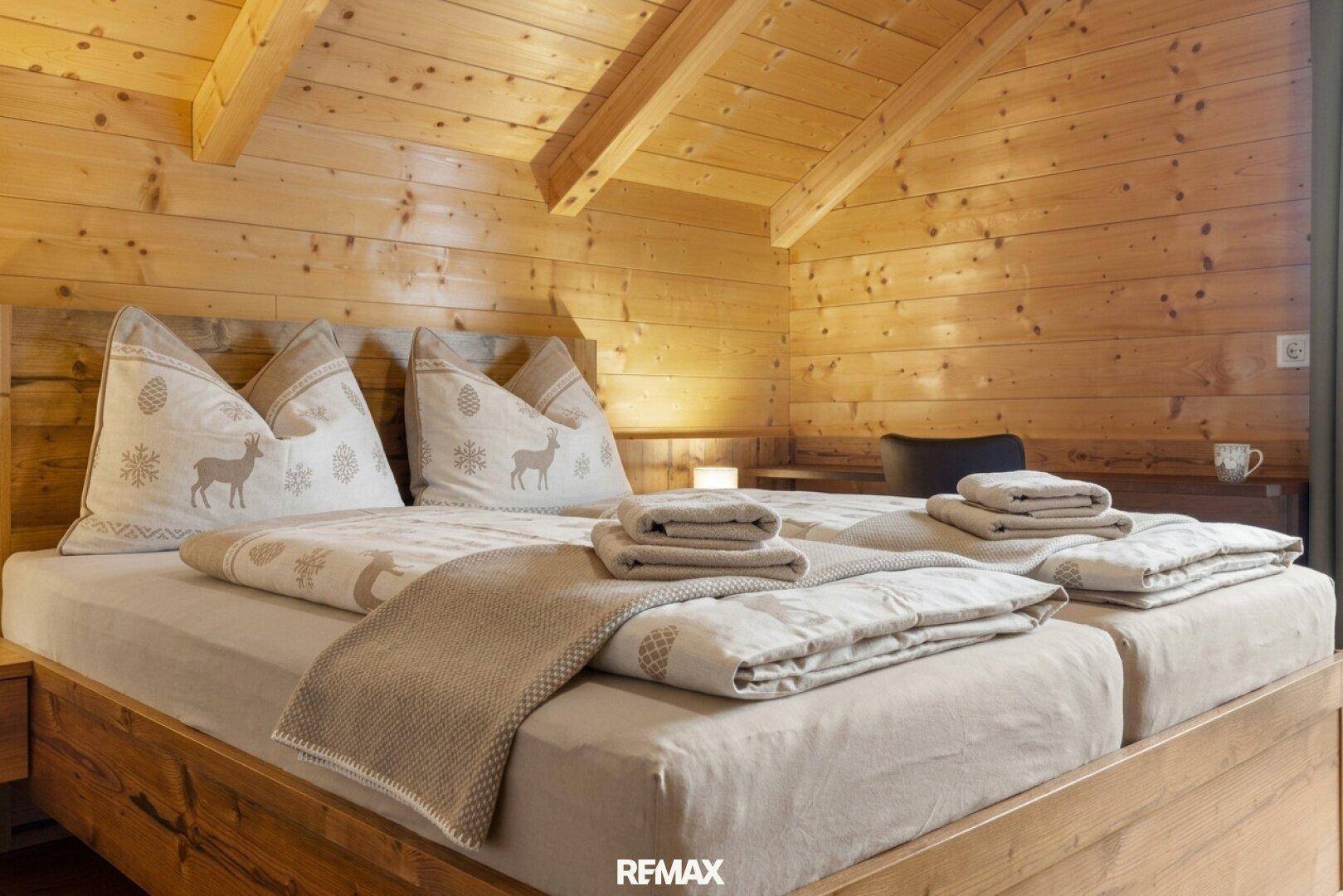 Detailansicht des Doppelbettes mit alpiner Bettwäsche und Holzkopfteil.