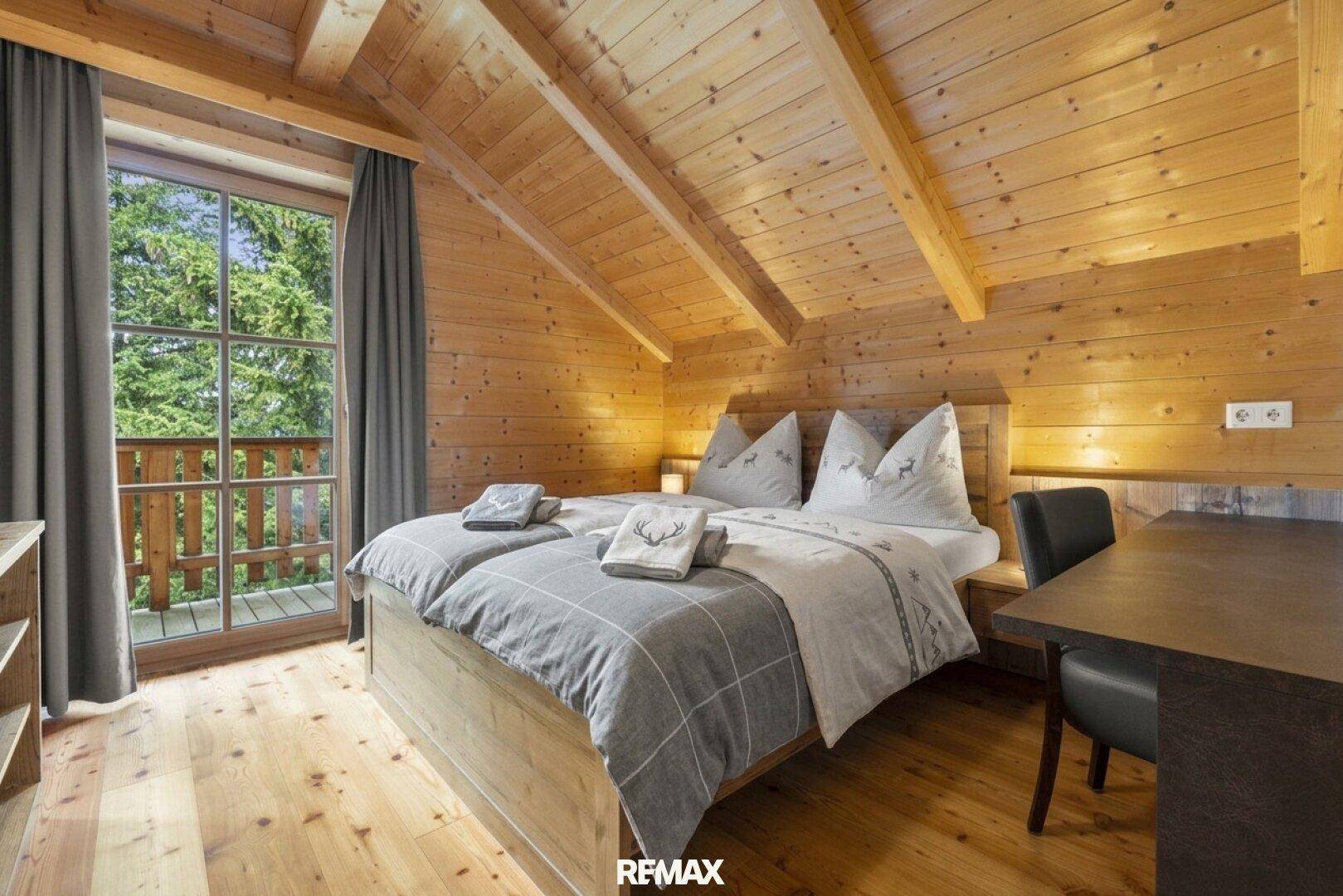 Helles Schlafzimmer mit Doppelbett, Holzwänden und direktem Zugang zum Balkon.