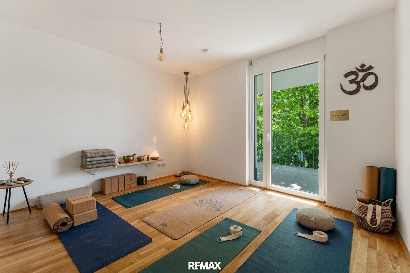 Heller Yogaraum mit Holzboden, Yogamatten und Blick ins Grüne durch die große Balkontür.