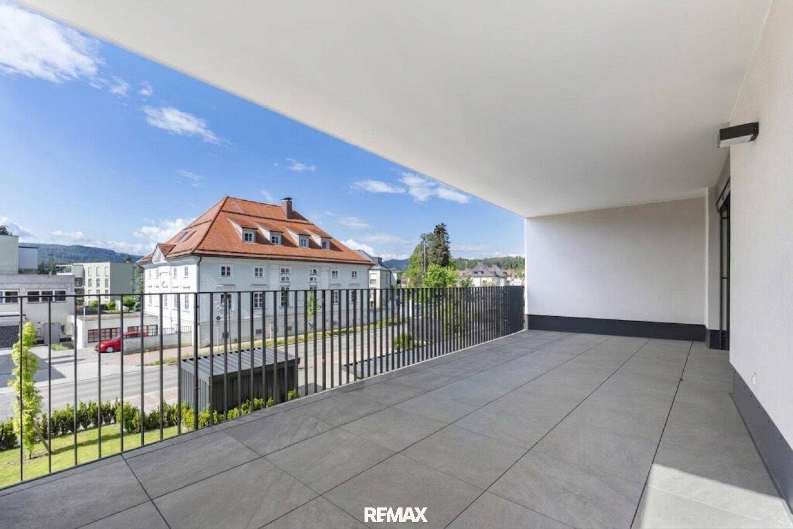 Geräumiger Balkon mit modernem Fliesenboden und weitem Blick über die Stadt und grüne Hügel.