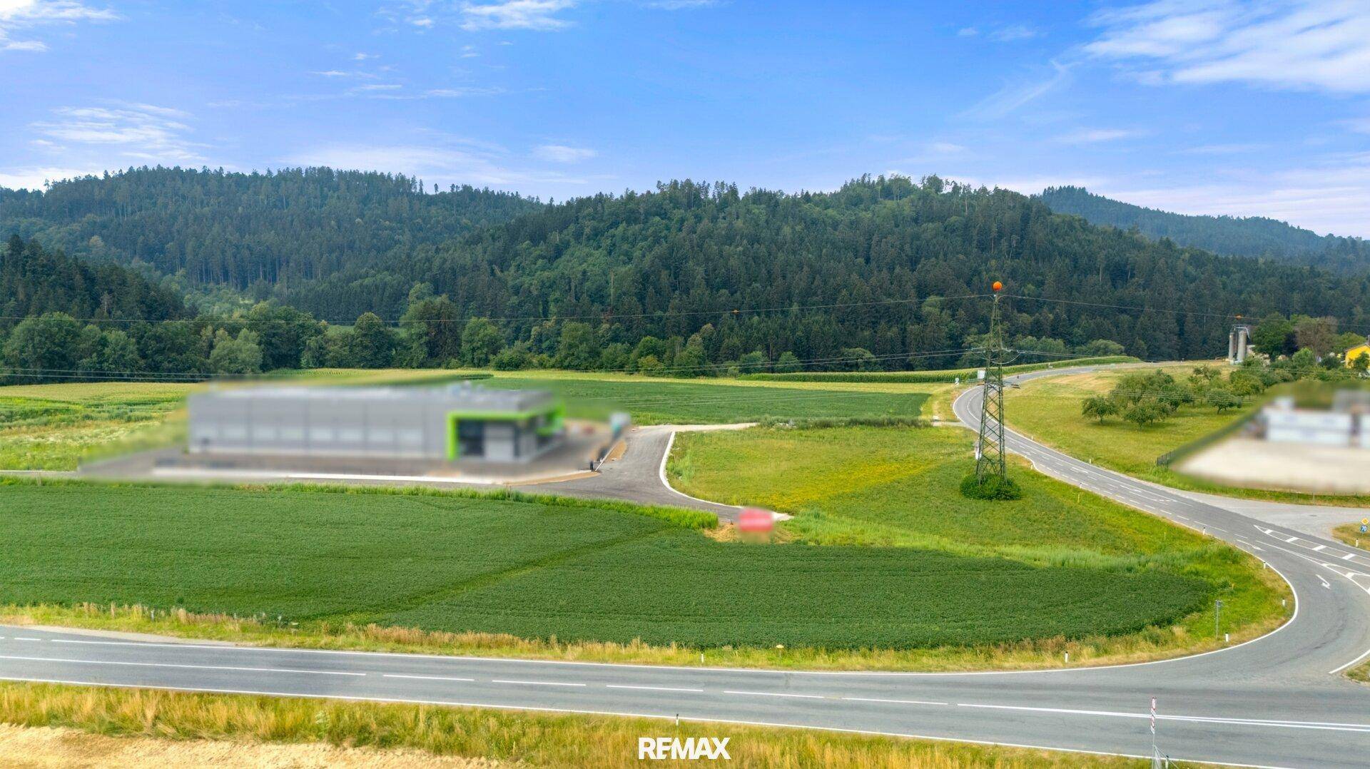 Panoramablick auf eine ländliche Landschaft mit einem modernen Gebäude, umgeben von Feldern und bewaldeten Hügeln.