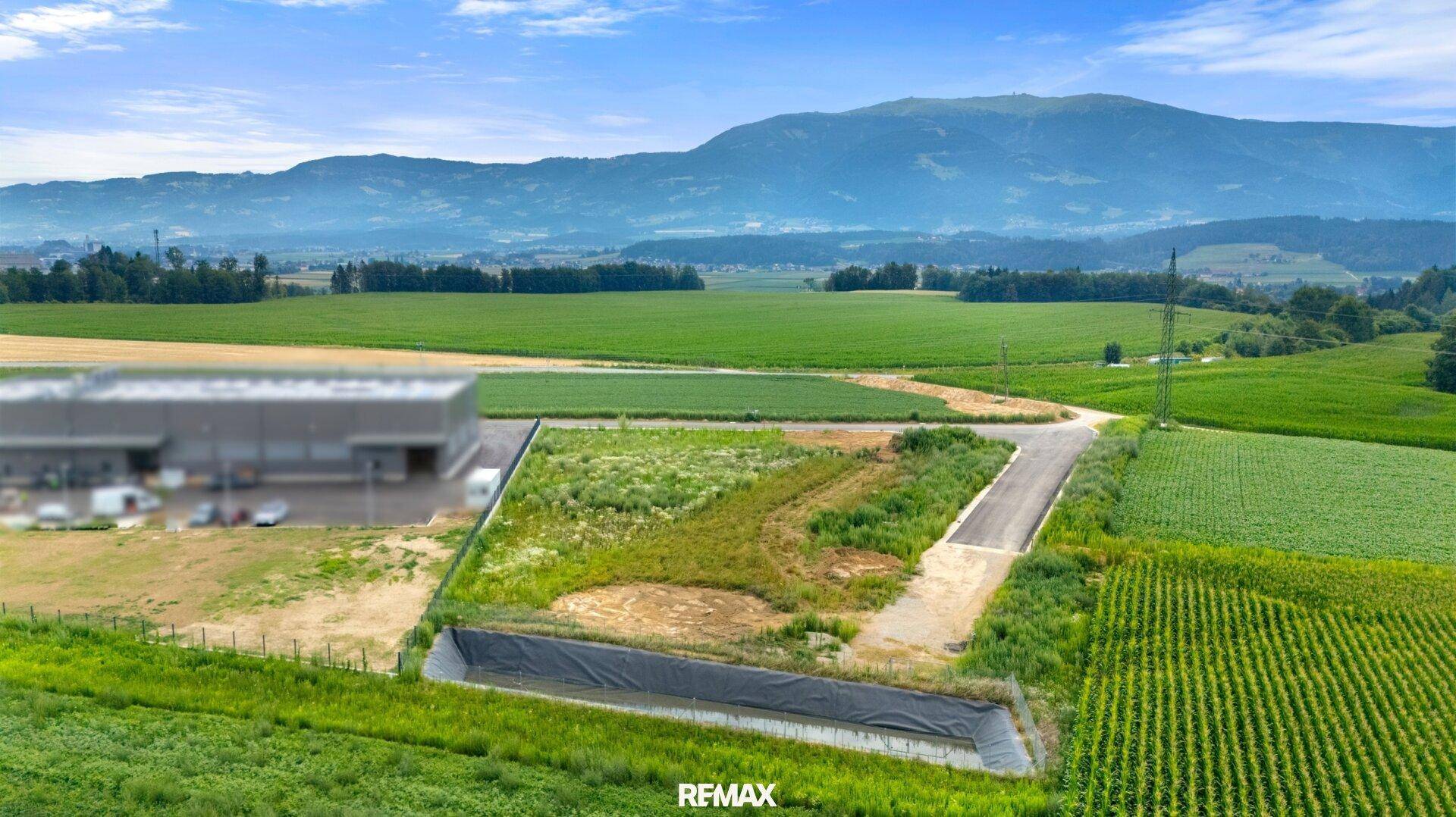 Weitwinkelaufnahme eines Grundstücks mit angrenzenden Feldern, einer Straße und einem Wasserbecken, umgeben von Natur.