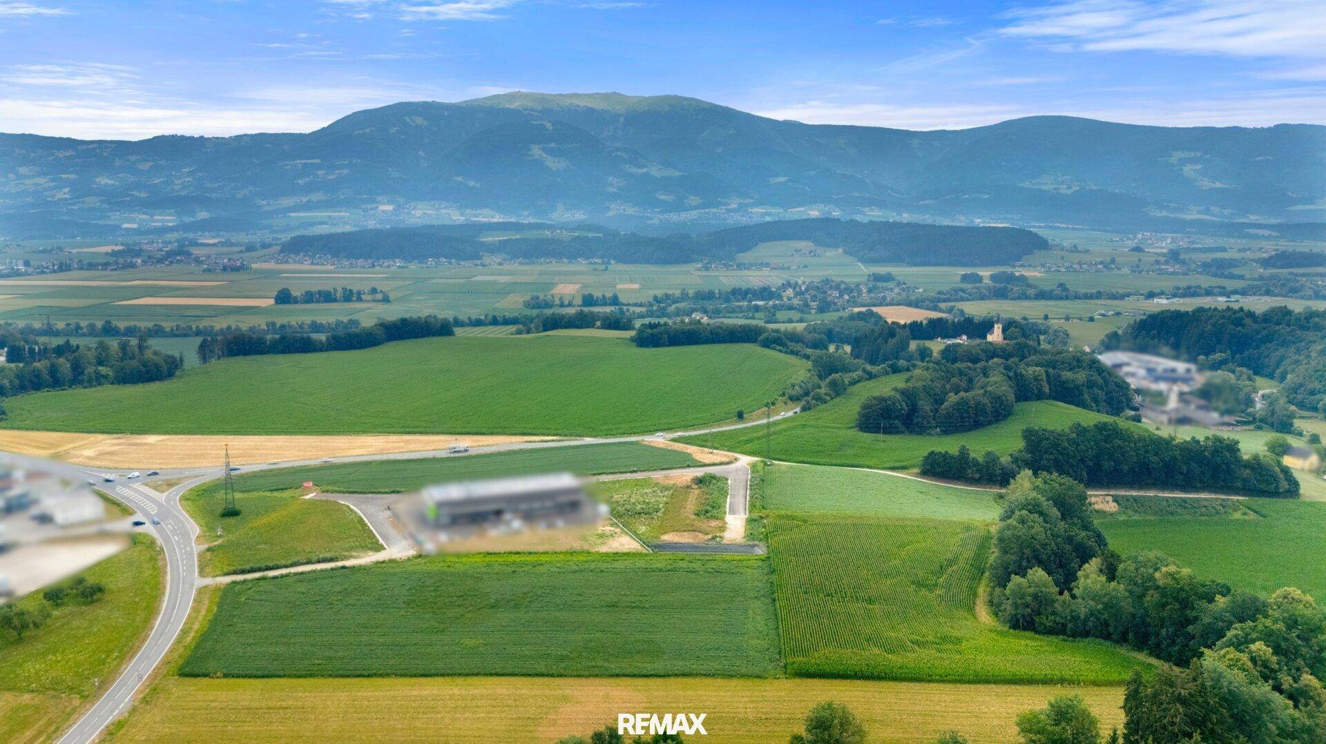 Luftaufnahme einer weiten Landschaft mit landwirtschaftlichen Flächen, Straßen und einer Bergkette.