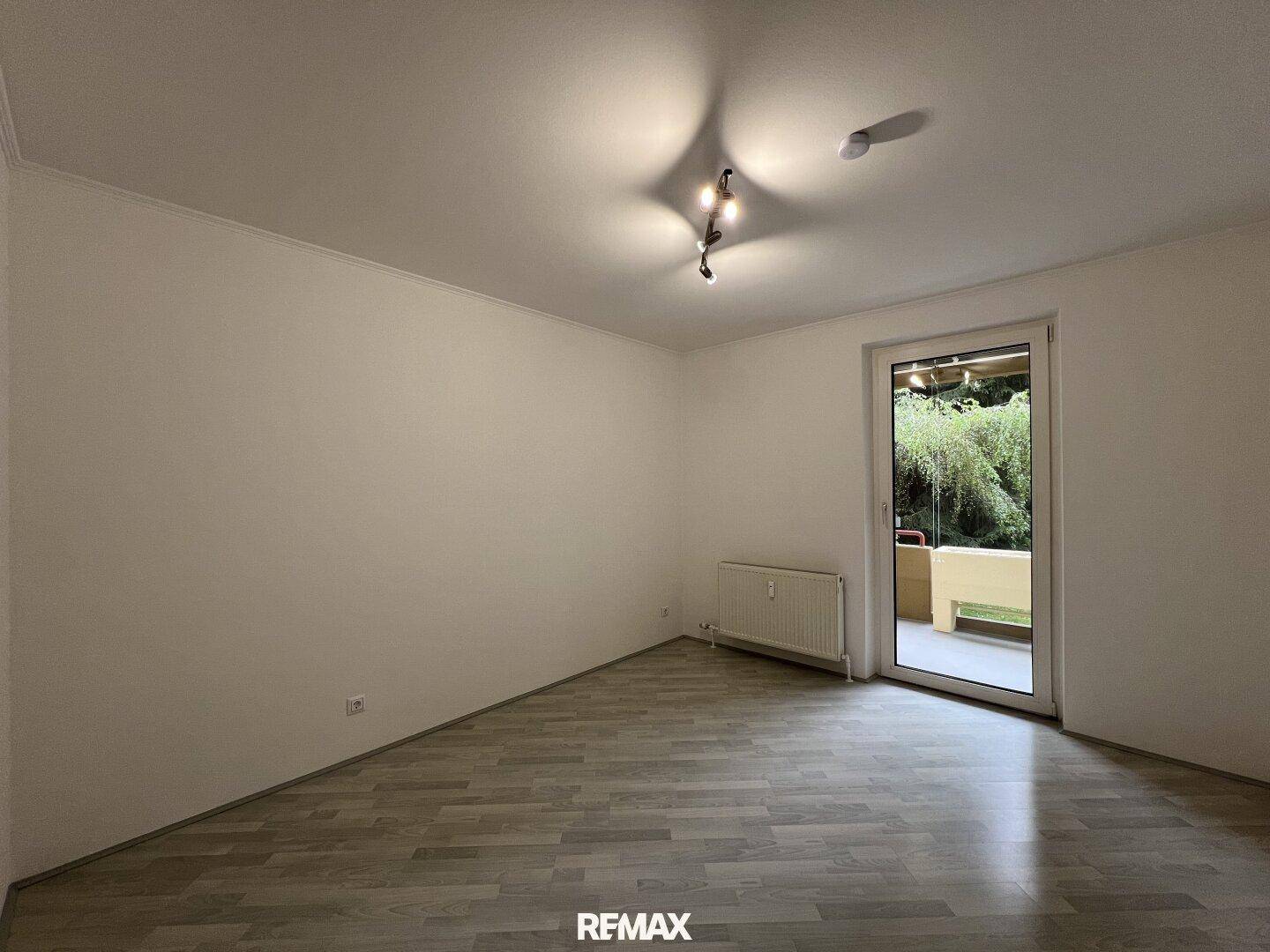 Geräumiges, unmöbliertes Schlafzimmer mit Laminatboden und direktem Balkonzugang.