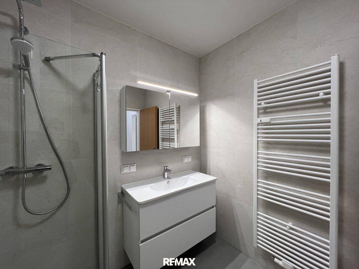 Modernes Badezimmer mit Duschbereich, Waschtisch und praktischem Handtuchheizkörper.