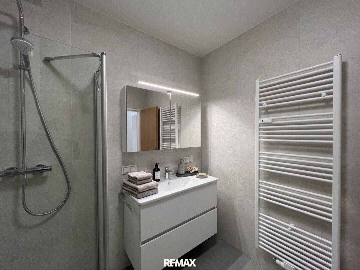 Modernes Badezimmer mit Dusche, Waschtischunterschrank und beheiztem Handtuchhalter.