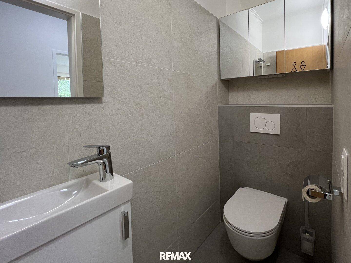 Helles Gäste-WC mit modernen grauen Fliesen, wandhängendem WC und Waschbecken.