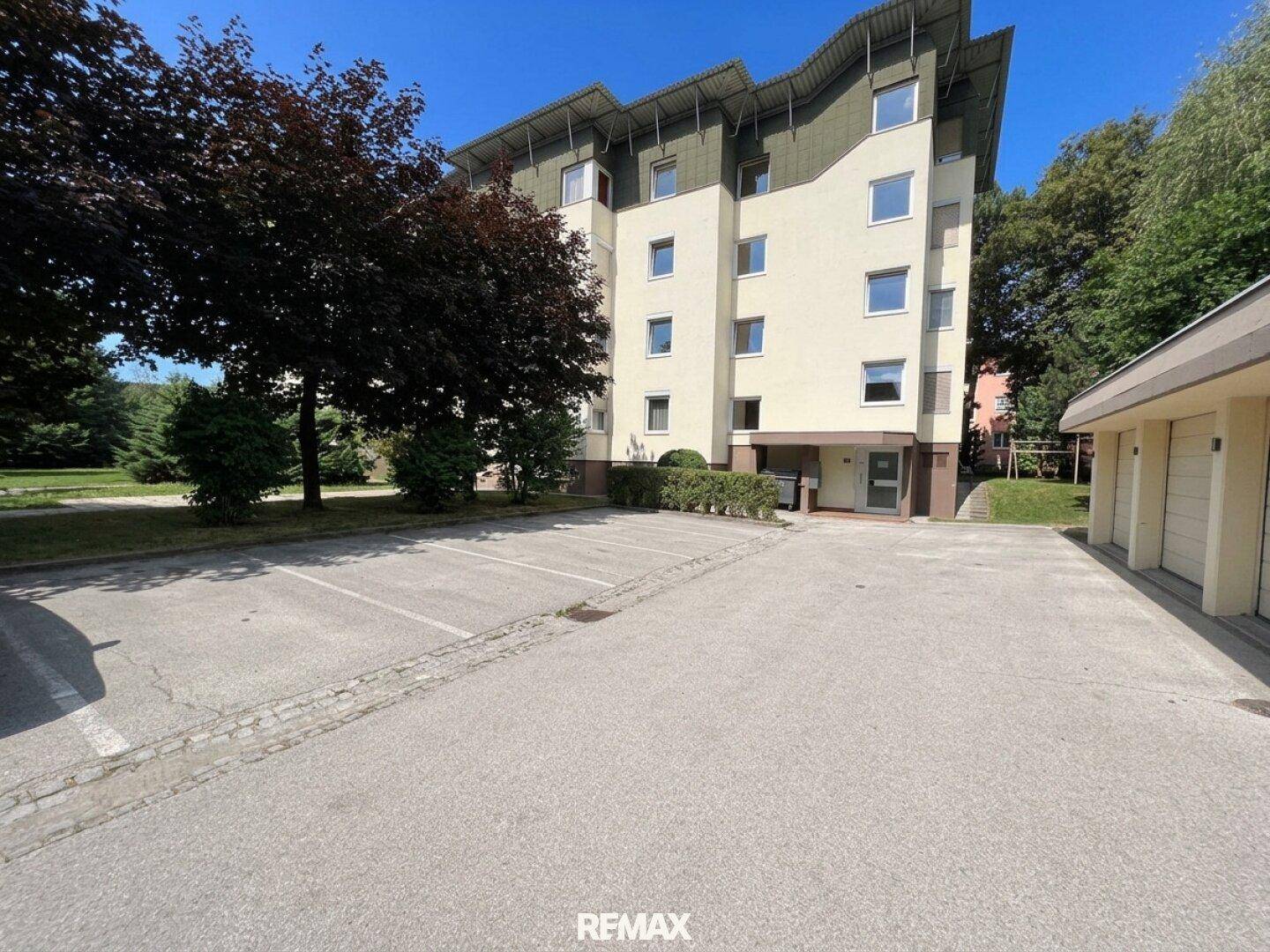 Mehrfamilienhaus mit Außenparkplätzen und umgebender Grünfläche an einem sonnigen Tag.
