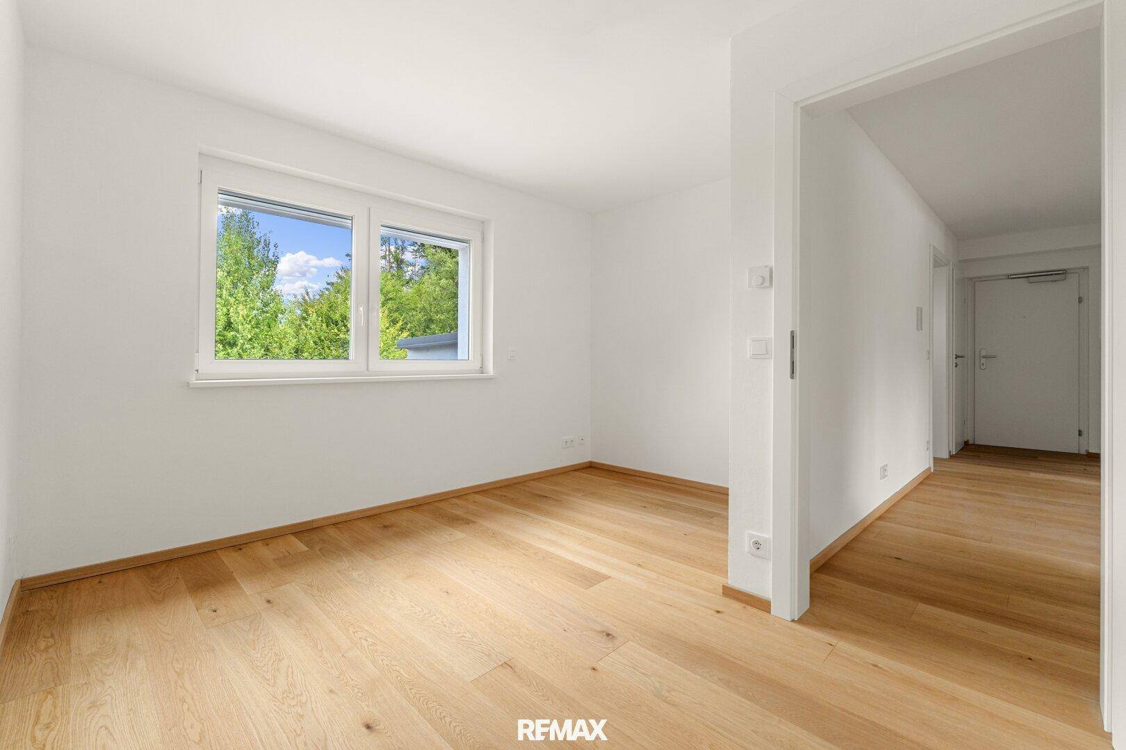 Helles Schlafzimmer mit Eichenparkett und Fenster mit Blick ins Grüne.