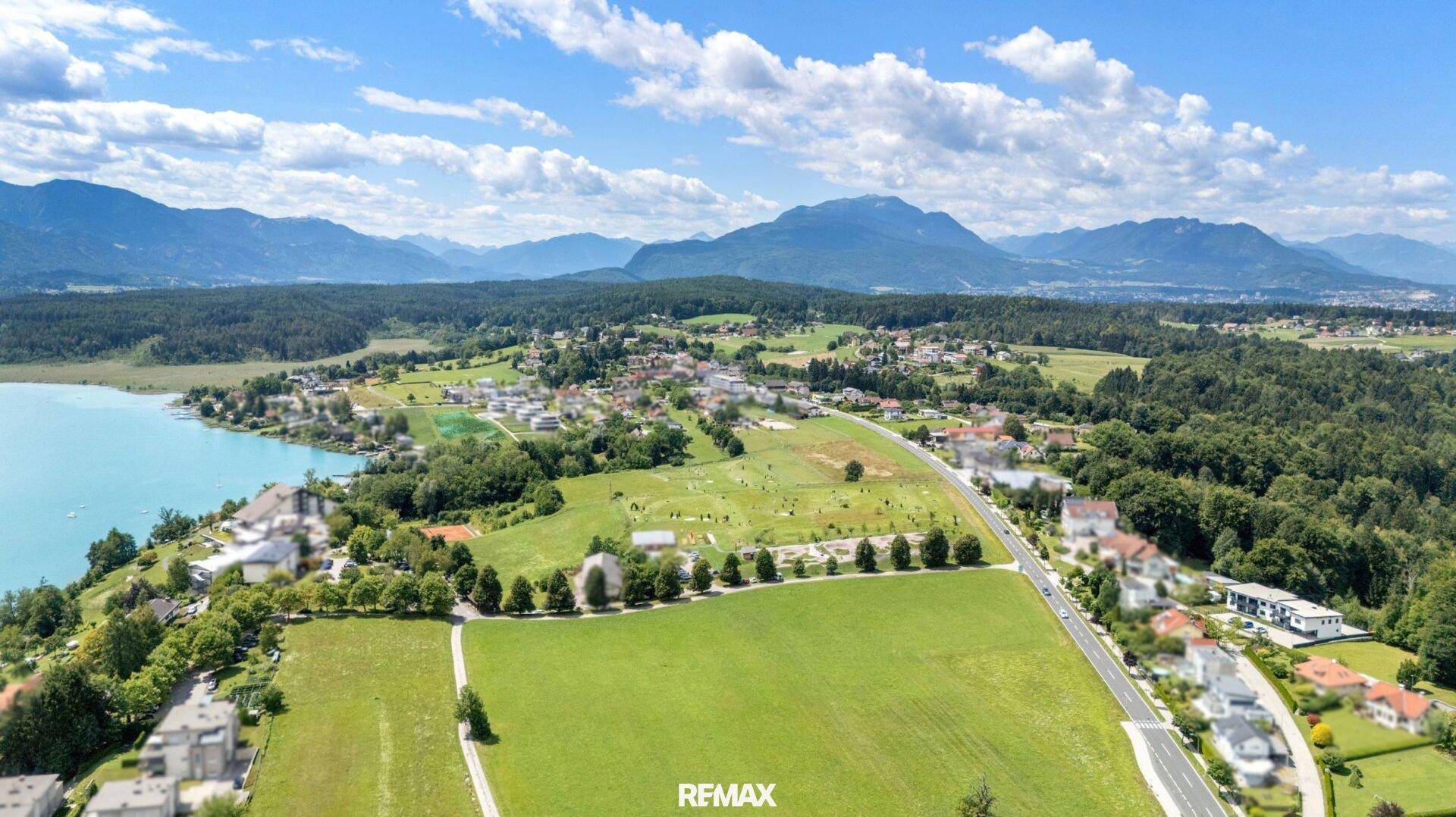 Weitläufige Luftaufnahme der Umgebung mit See, grünen Feldern und Bergen im Hintergrund.