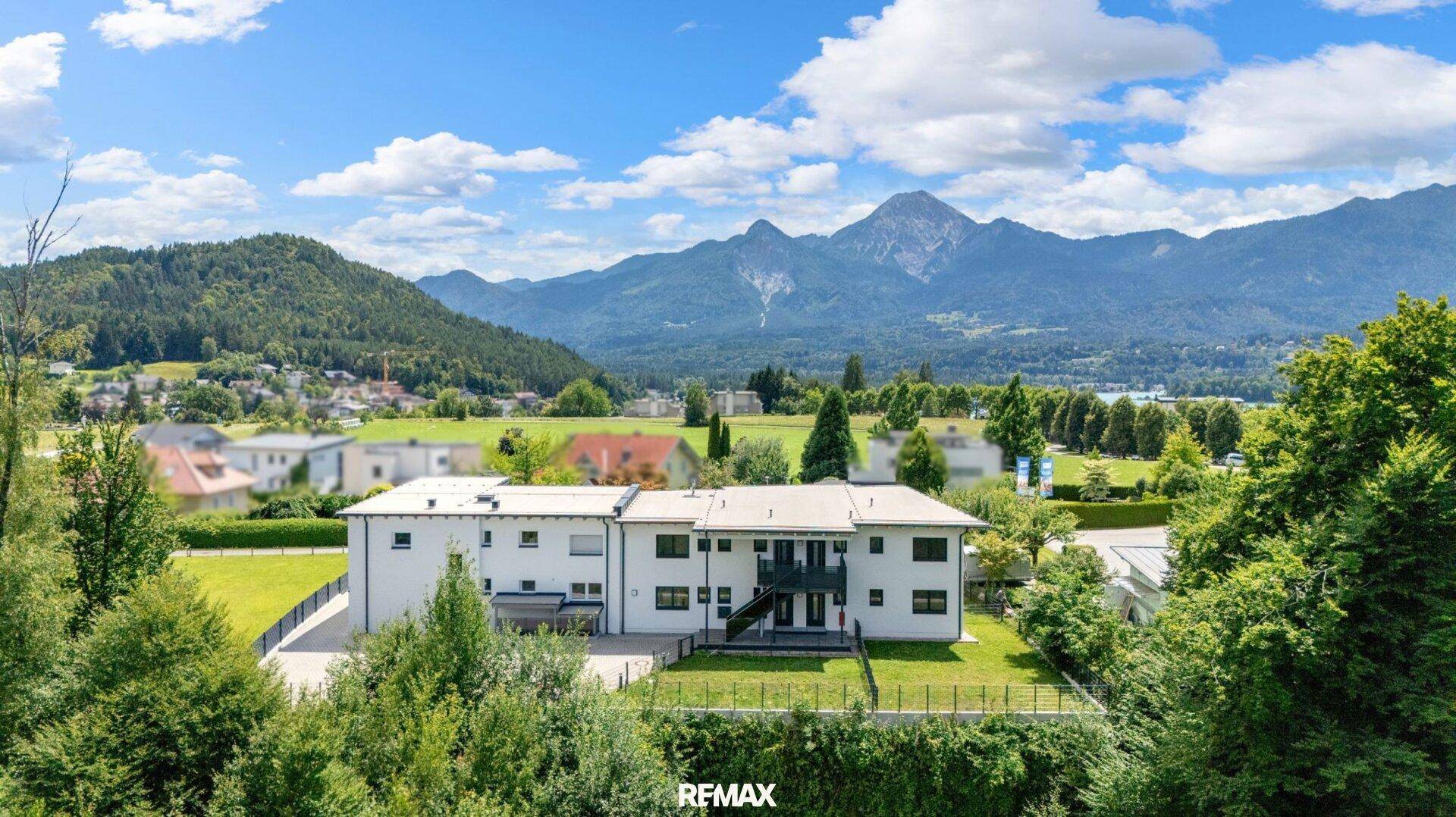 Luftaufnahme eines modernen Gebäudes mit umliegender Natur und Bergblick im Hintergrund.