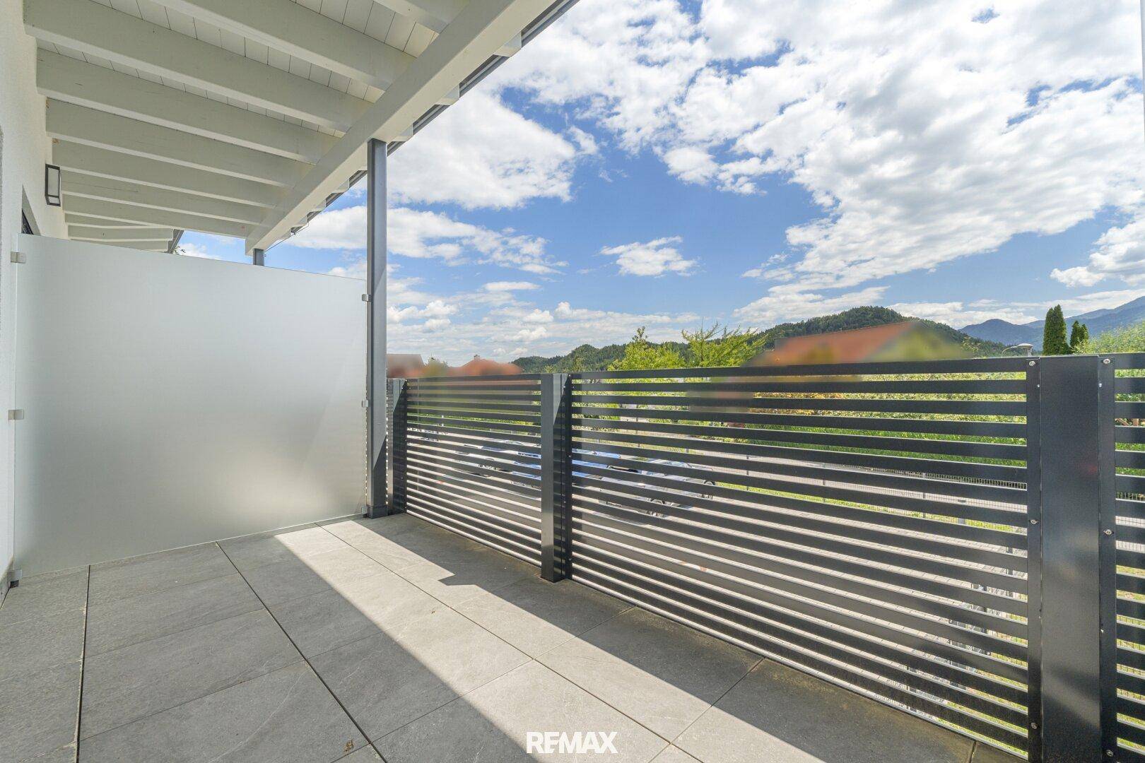 Überdachter Balkon mit Fliesenboden, modernem Sichtschutz und weitem Blick in die Natur.