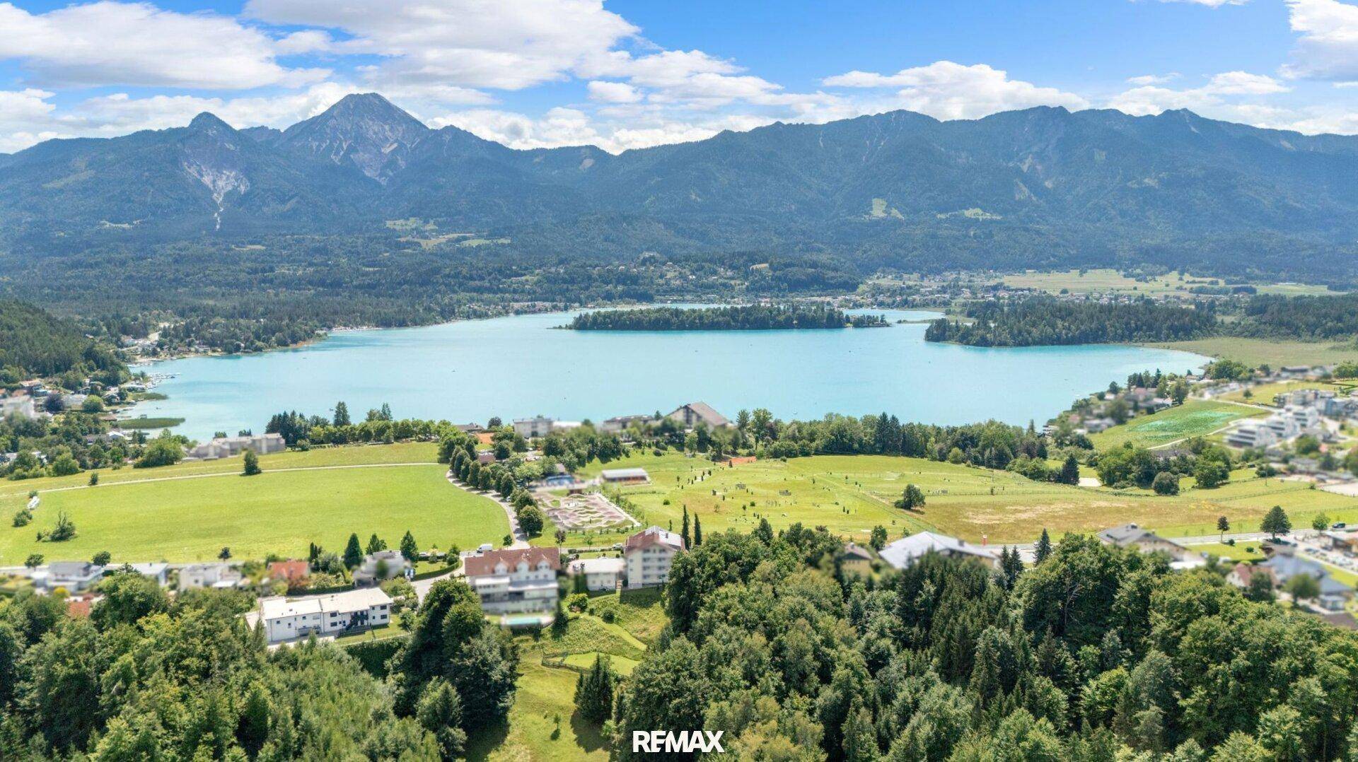 Panoramablick auf den See und die umliegende Berglandschaft unter blauem Himmel.