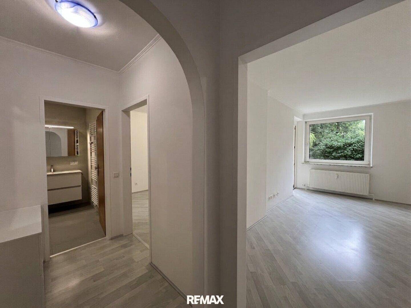Heller Flur mit Zugang zu einem modernen Badezimmer und einem weiteren Zimmer mit Laminatboden und Fenster.