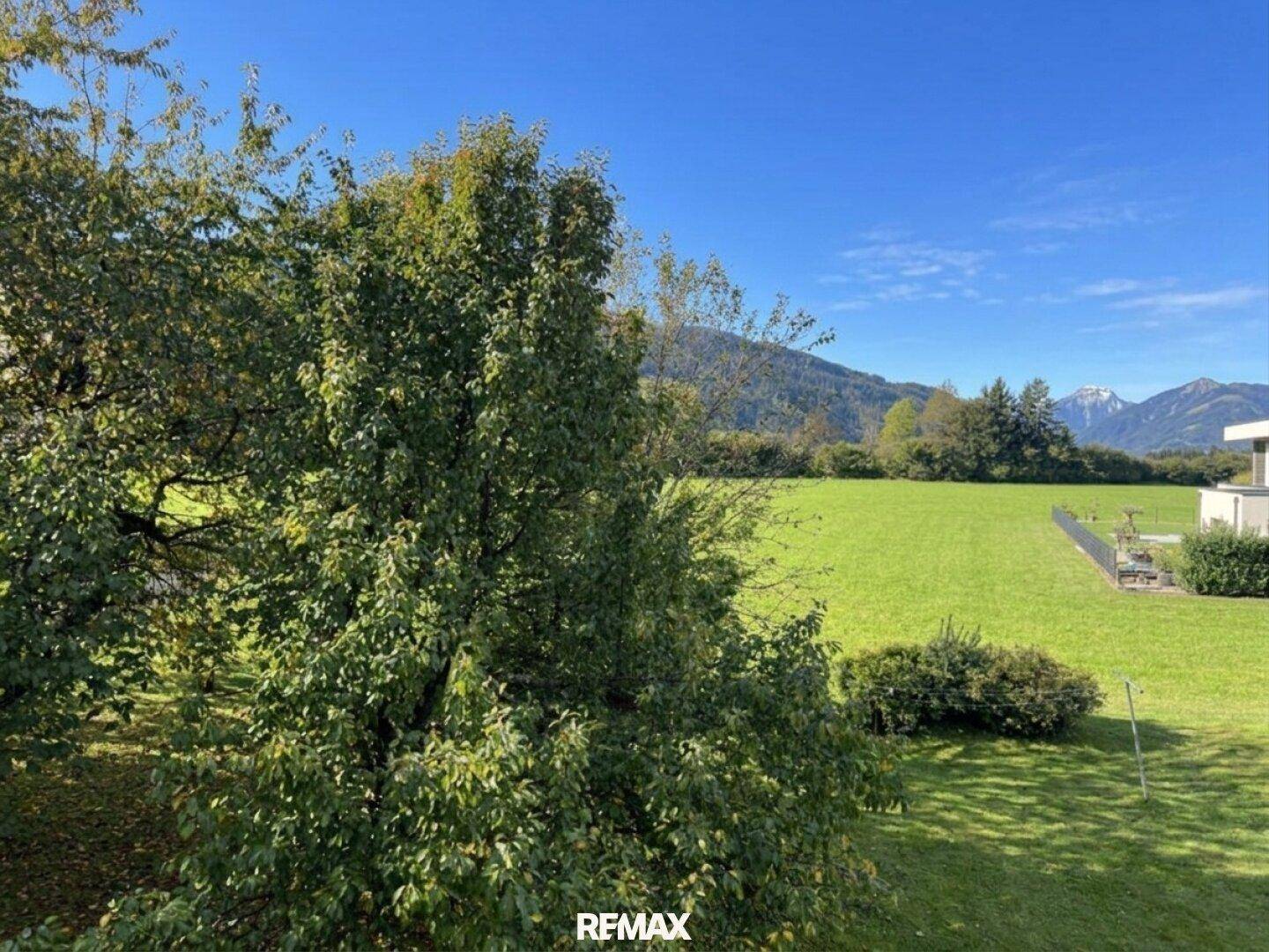 Panoramablick über grüne Felder und die umliegende Berglandschaft unter blauem Himmel.