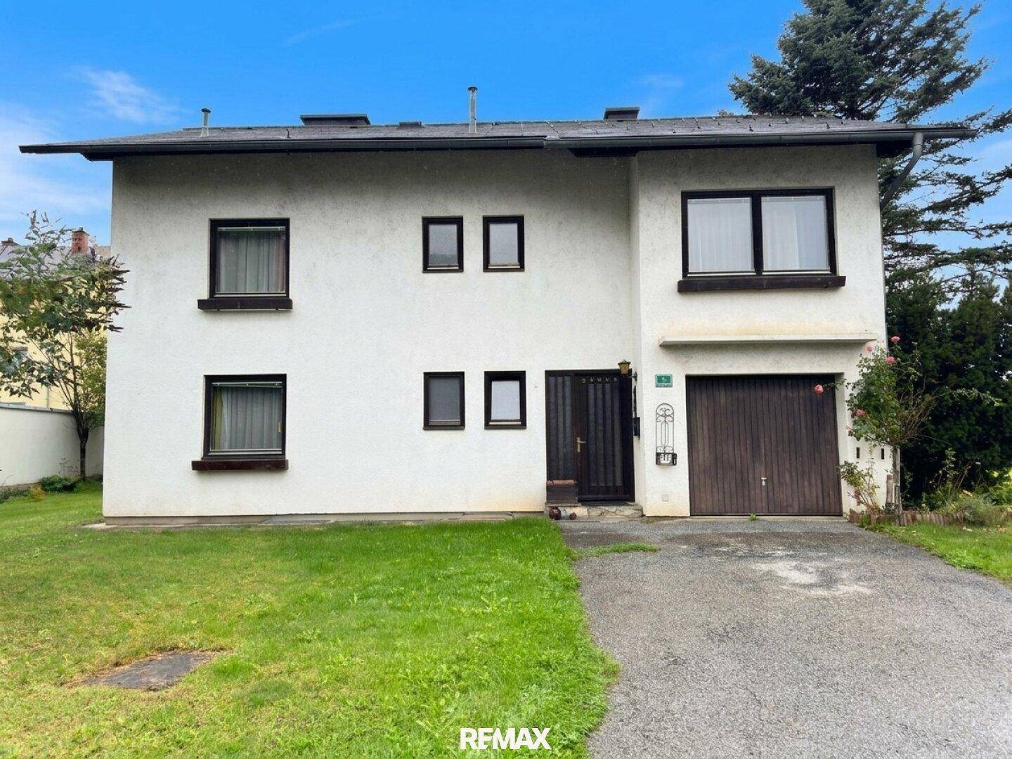 Vorderansicht des Einfamilienhauses mit Garage, Einfahrt und Vorgarten unter blauem Himmel.