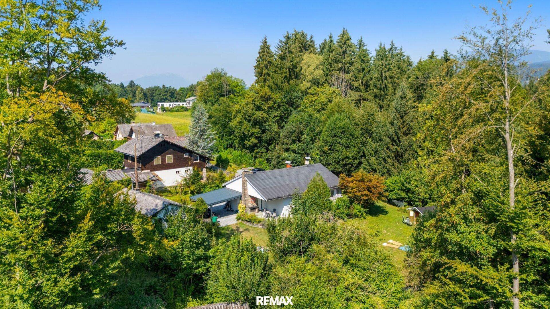 Haus eingebettet in eine grüne, waldreiche Umgebung mit weiteren Häusern in der Nähe.