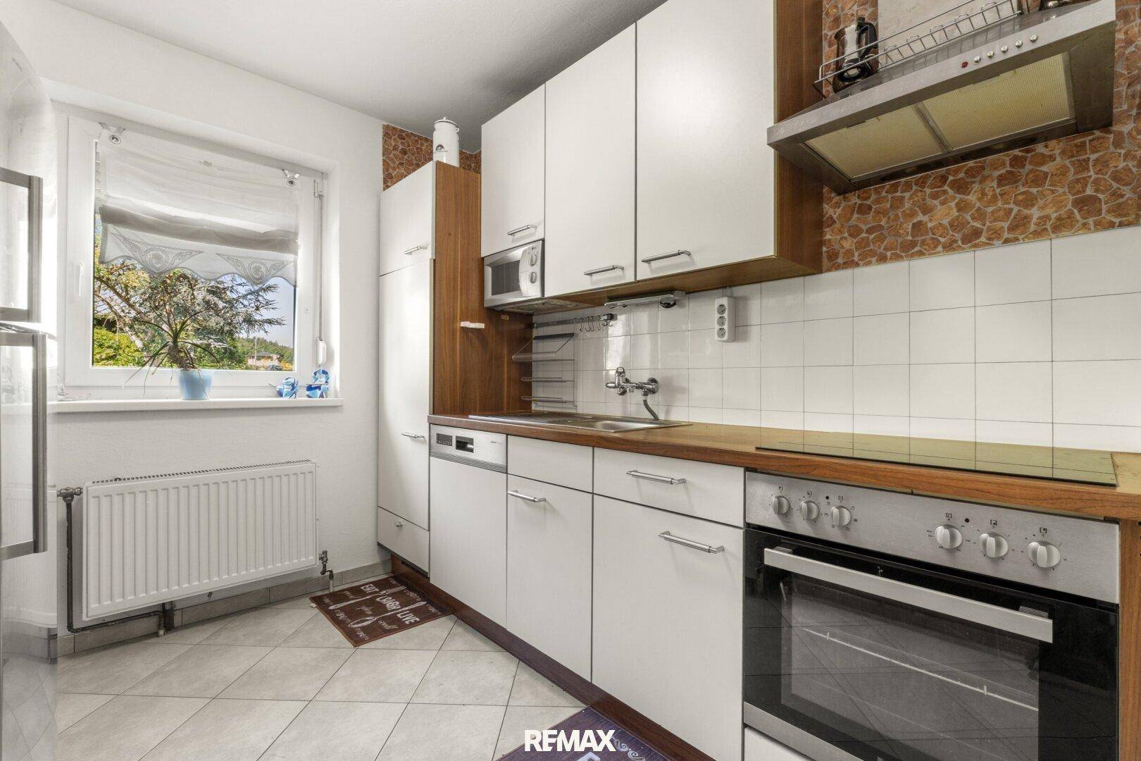 Funktionale Küche mit weißen Schränken, Holztheke und Fenster für natürliches Licht.
