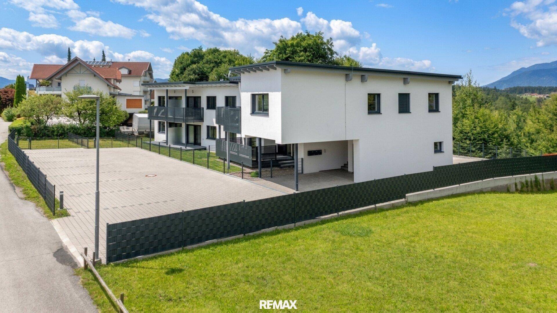 Moderne Wohnanlage mit weißer Fassade, großem Parkplatz und grüner Umgebung.