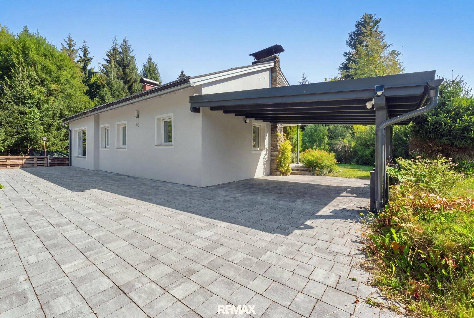 Seitenansicht des Hauses mit gepflasterter Einfahrt und überdachtem Carport.