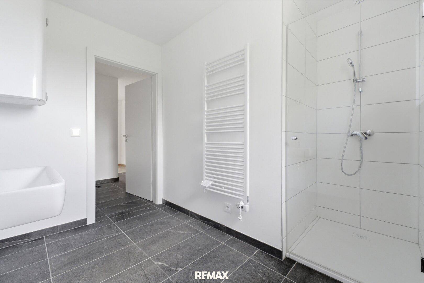 Modernes Badezimmer mit dunklen Fliesen, Duschkabine und beheiztem Handtuchhalter.