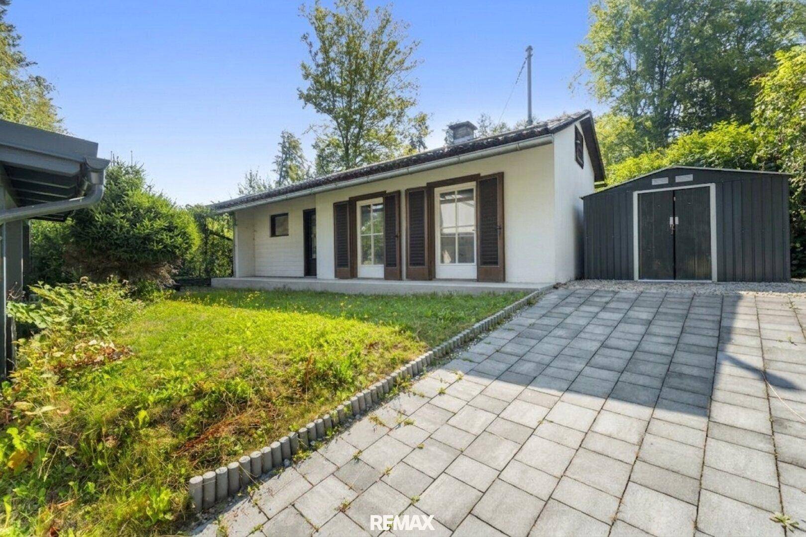 Hausansicht mit gepflasterter Einfahrt, Garten und praktischem Geräteschuppen.