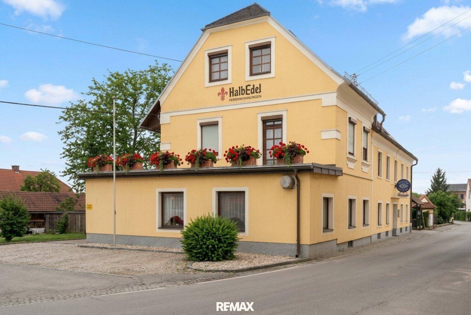 Traditionelles gelbes Gebäude mit Giebeldach, Fensterläden und Blumenkästen an einer ruhigen Straße gelegen.