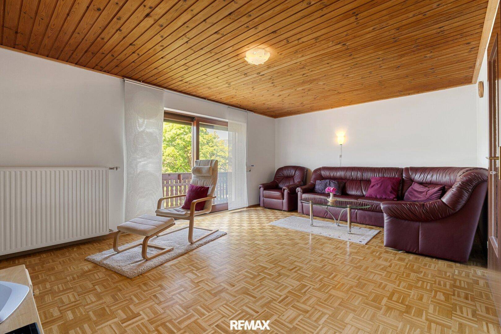 Gemütliches Wohnzimmer mit Holzdecke, Parkettboden und Zugang zum Balkon.