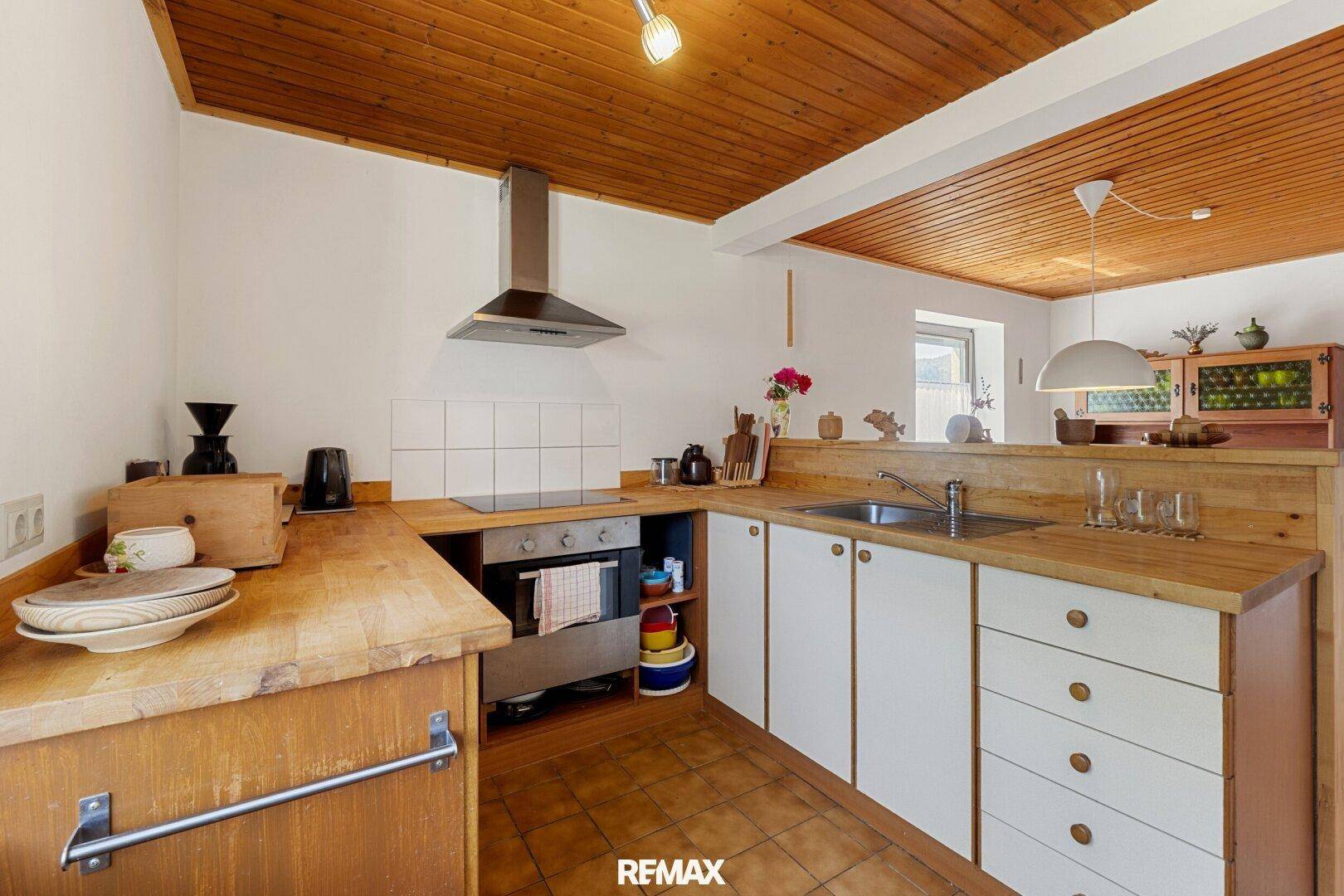 Funktionale Küche mit Holz-Arbeitsplatten, weißen Unterschränken und Fliesenboden.