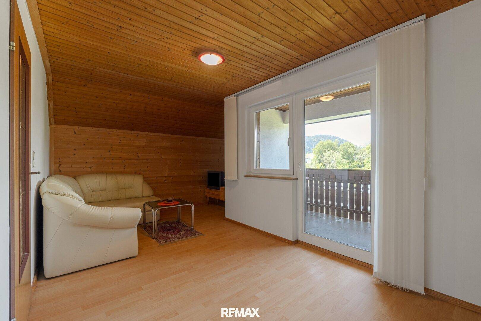 Wohnzimmer im Dachgeschoss mit Holzdecke, Laminatboden und Zugang zum Balkon.