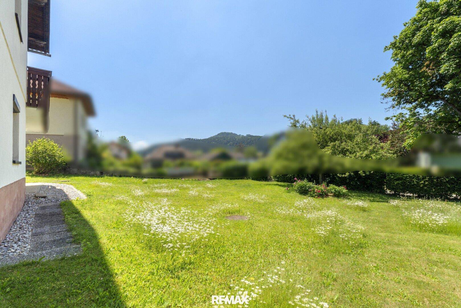 Großer, gepflegter Garten mit Rasenfläche und Blumen, umgeben von grüner Natur.