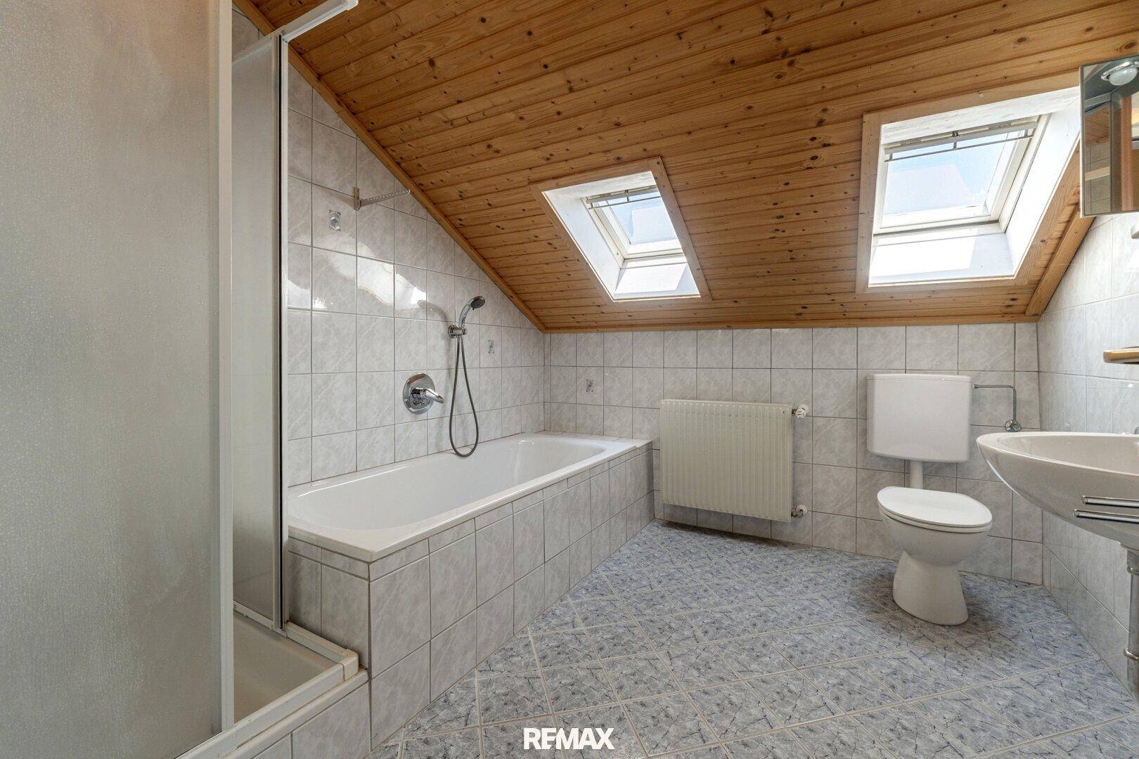 Gefliestes Badezimmer im Dachgeschoss mit Badewanne, Dusche und Dachfenstern.