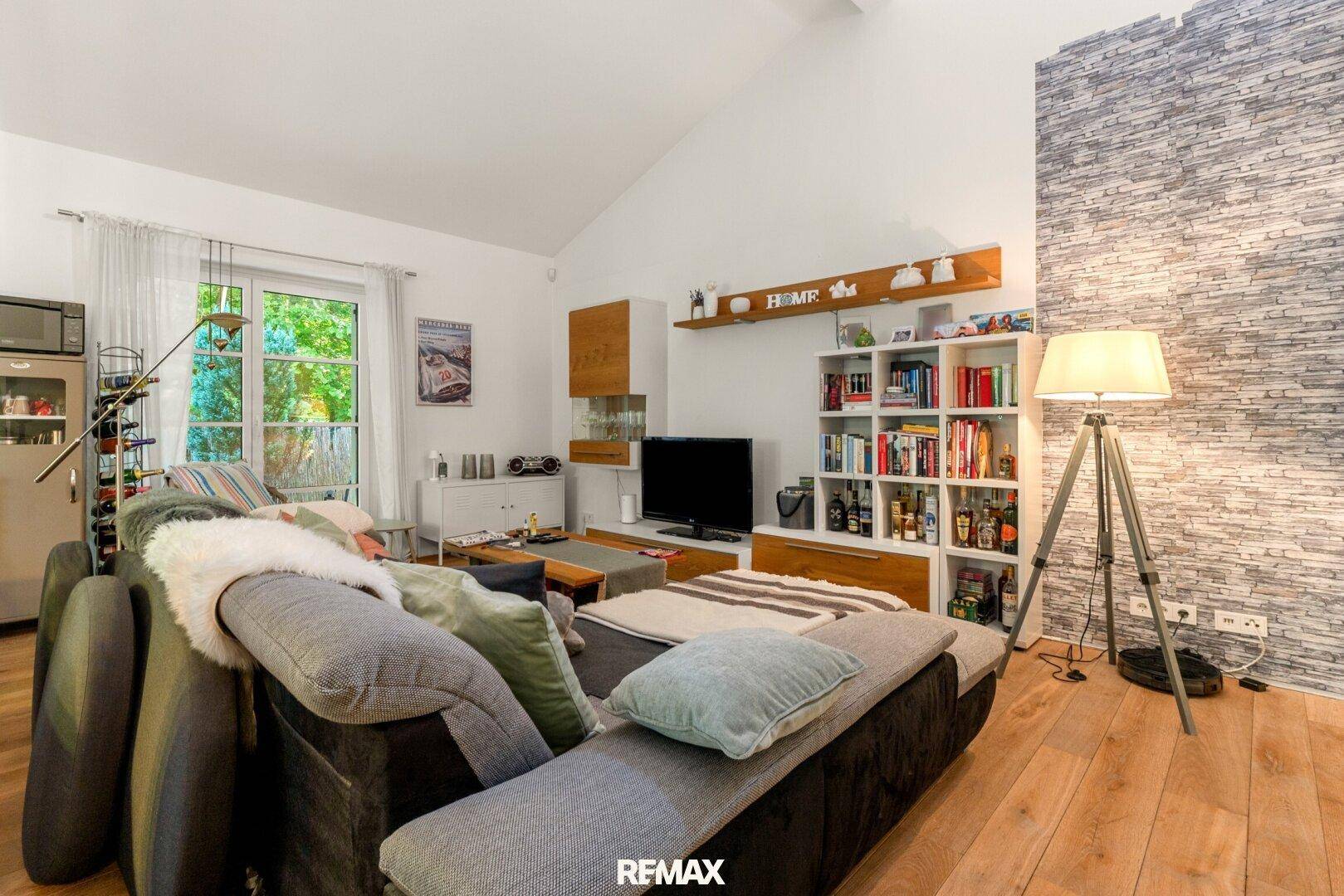 Heller Wohnbereich mit großem Sofa, Bücherregal und Zugang zum Garten.