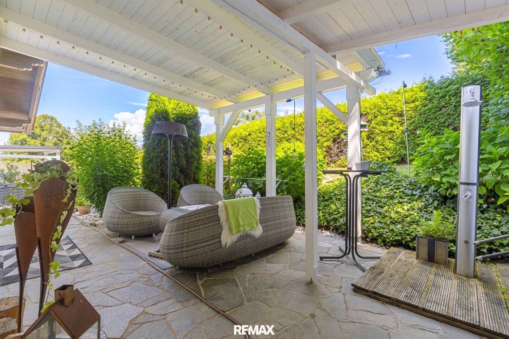 Überdachte Terrasse mit gemütlichen Loungemöbeln und Steinboden im Garten.