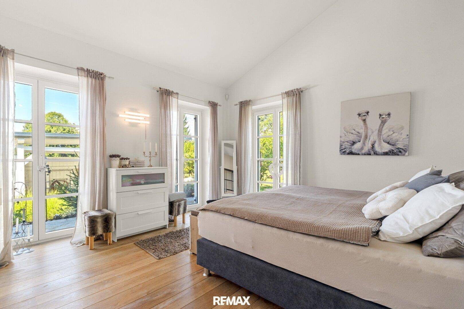 Helles Schlafzimmer mit mehreren Fenstern, Holzboden und Zugang zum Außenbereich.