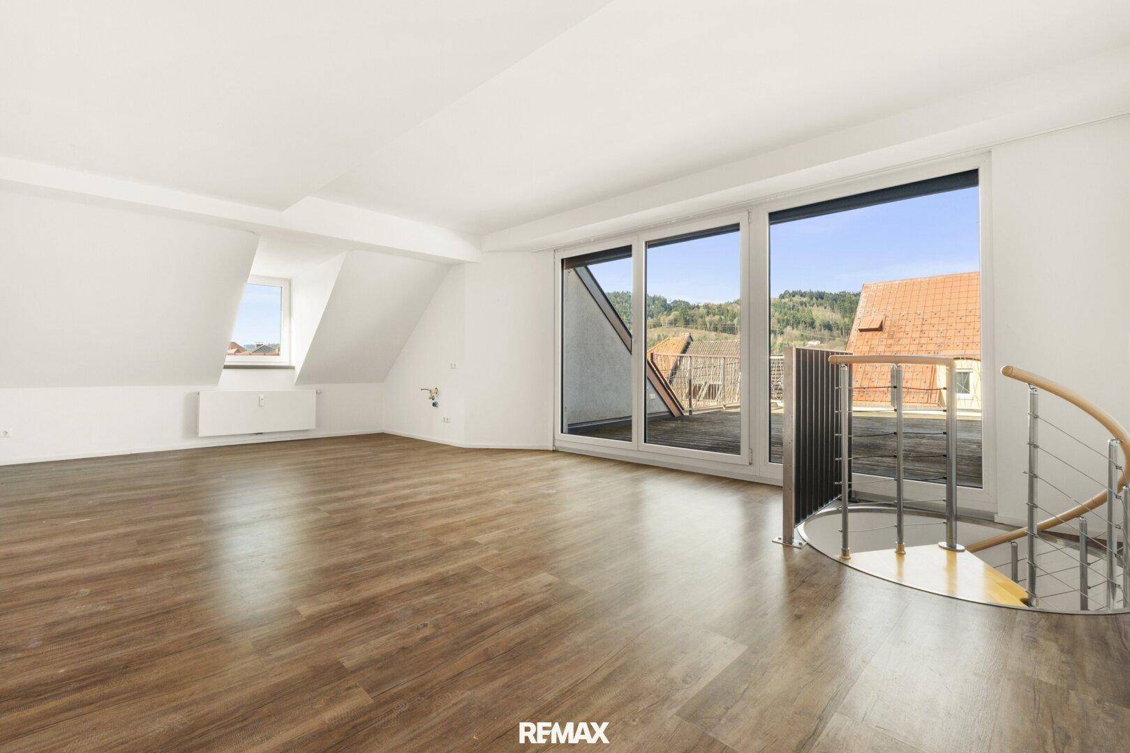 Helles Wohnzimmer im Dachgeschoss mit Laminatboden, großen Fenstern und Zugang zur Dachterrasse.